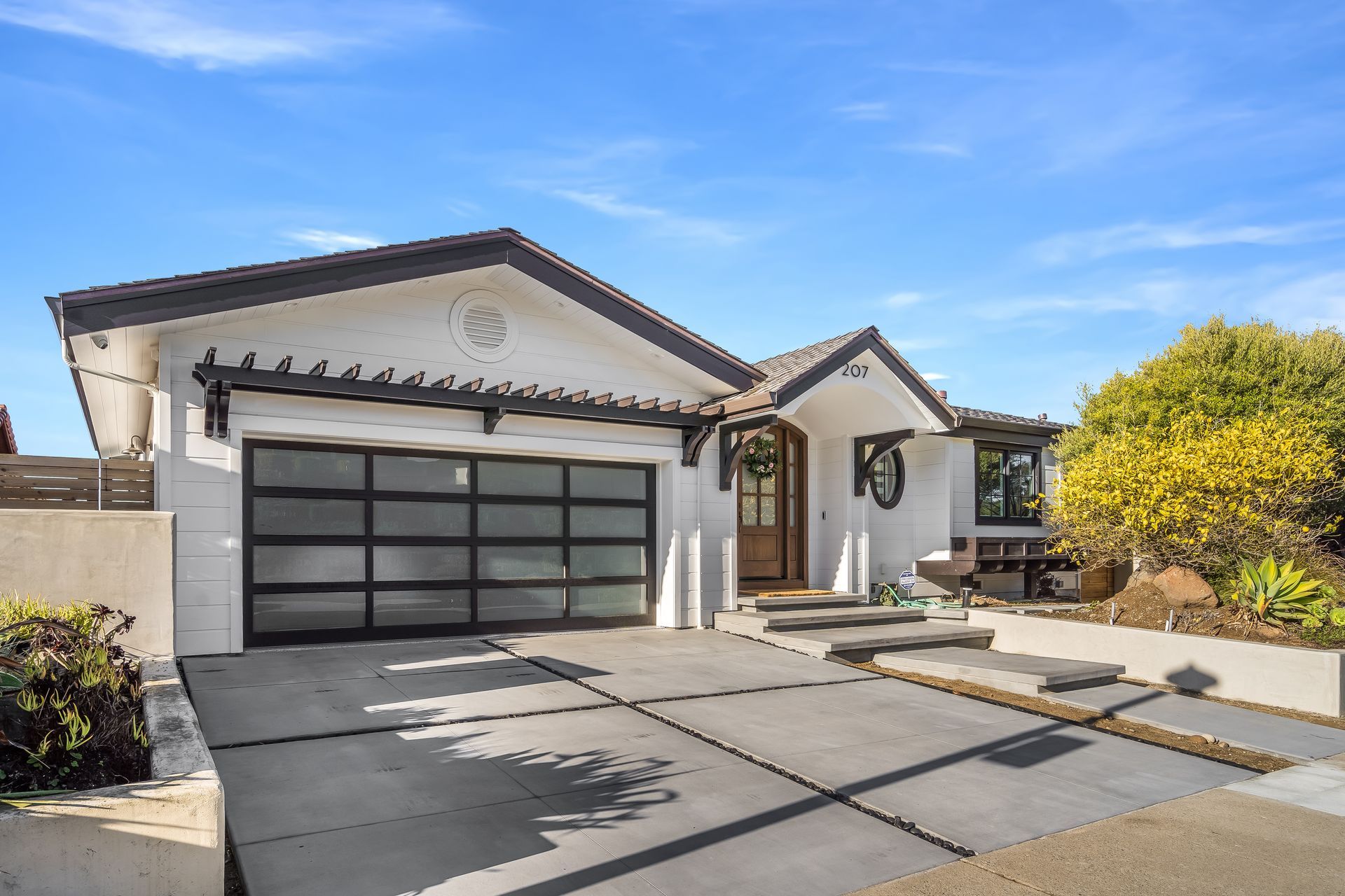 White house with black trim, glass garage door, steps up to front door, blue sky.