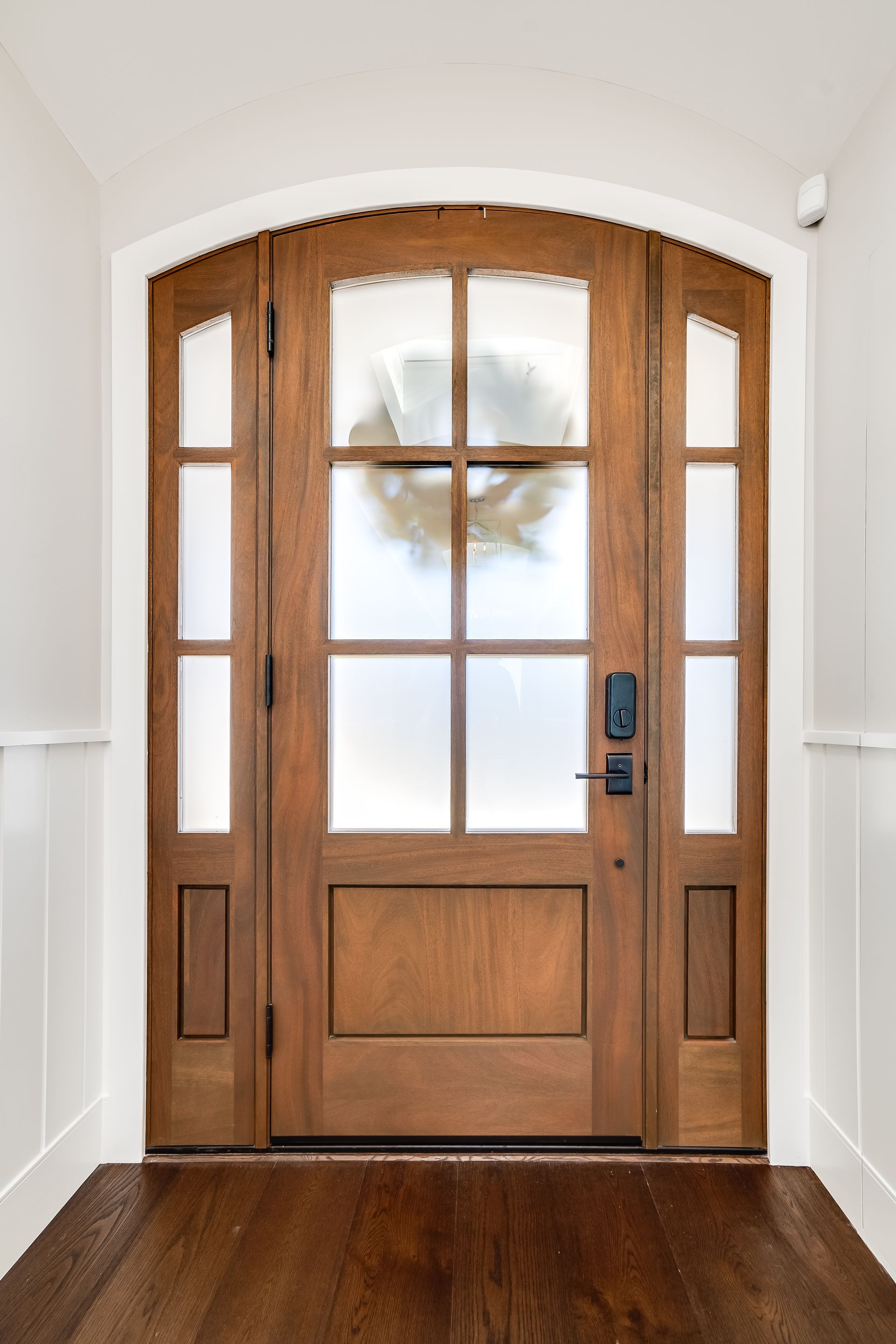 Wooden front door with frosted glass panels, a wreath, and a smart lock.