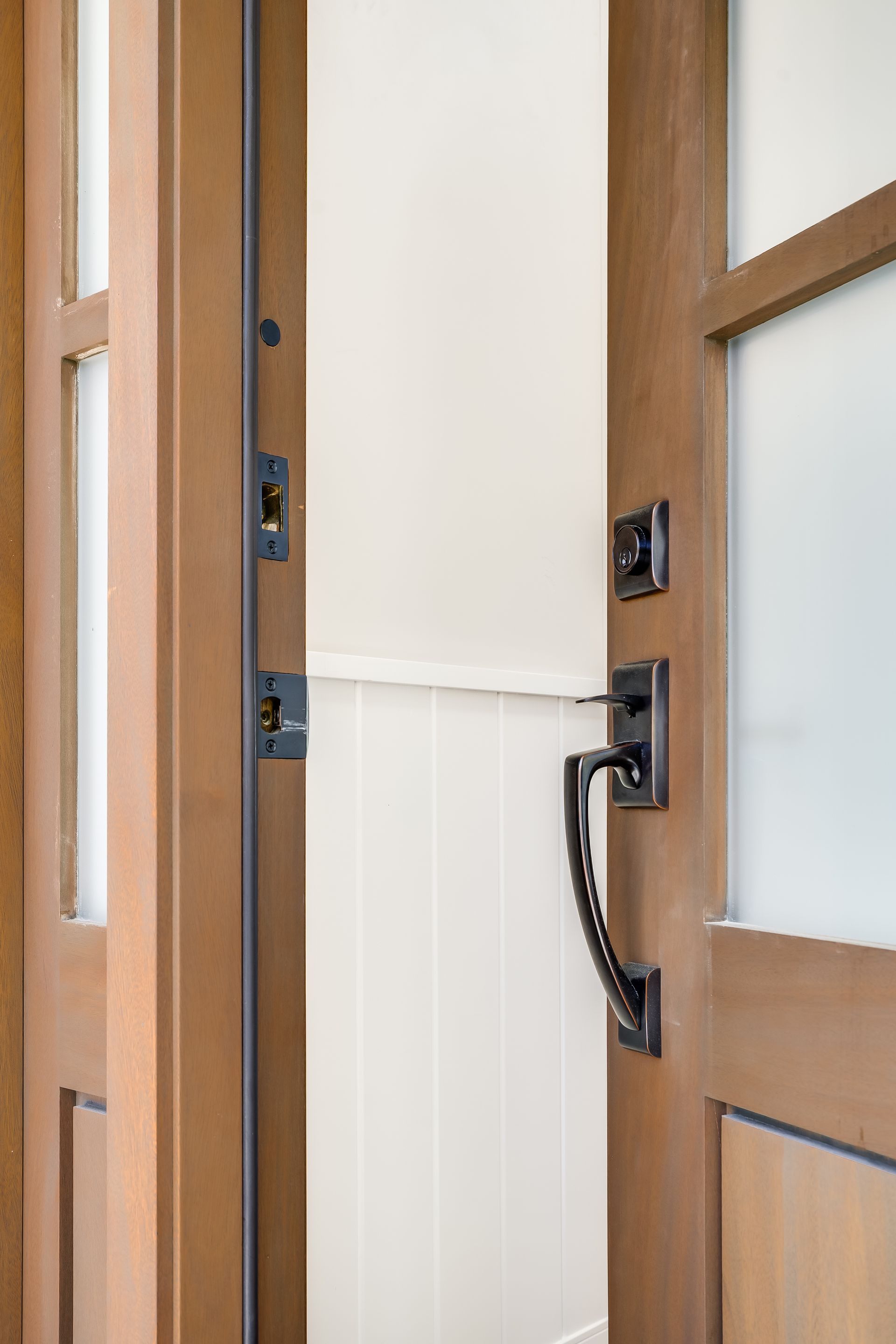 Wooden door ajar, revealing a white wall with a black handle and lock.