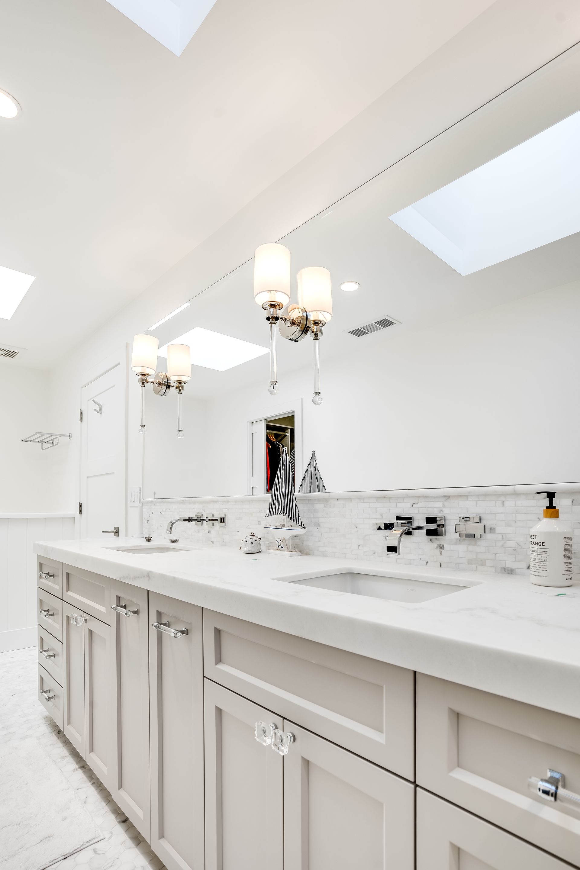 White bathroom with double vanity, large mirror, and two skylights.
