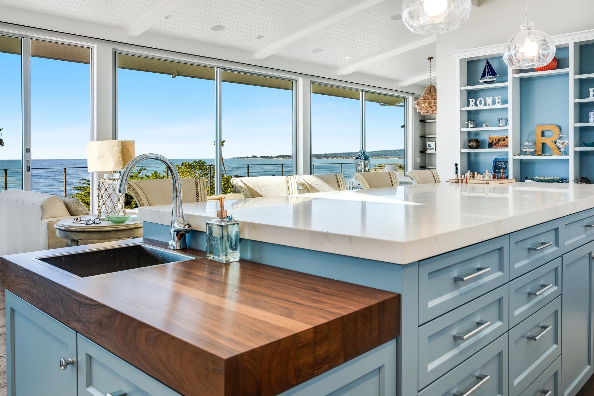 Coastal kitchen with blue cabinets, wooden countertops, and ocean view.
