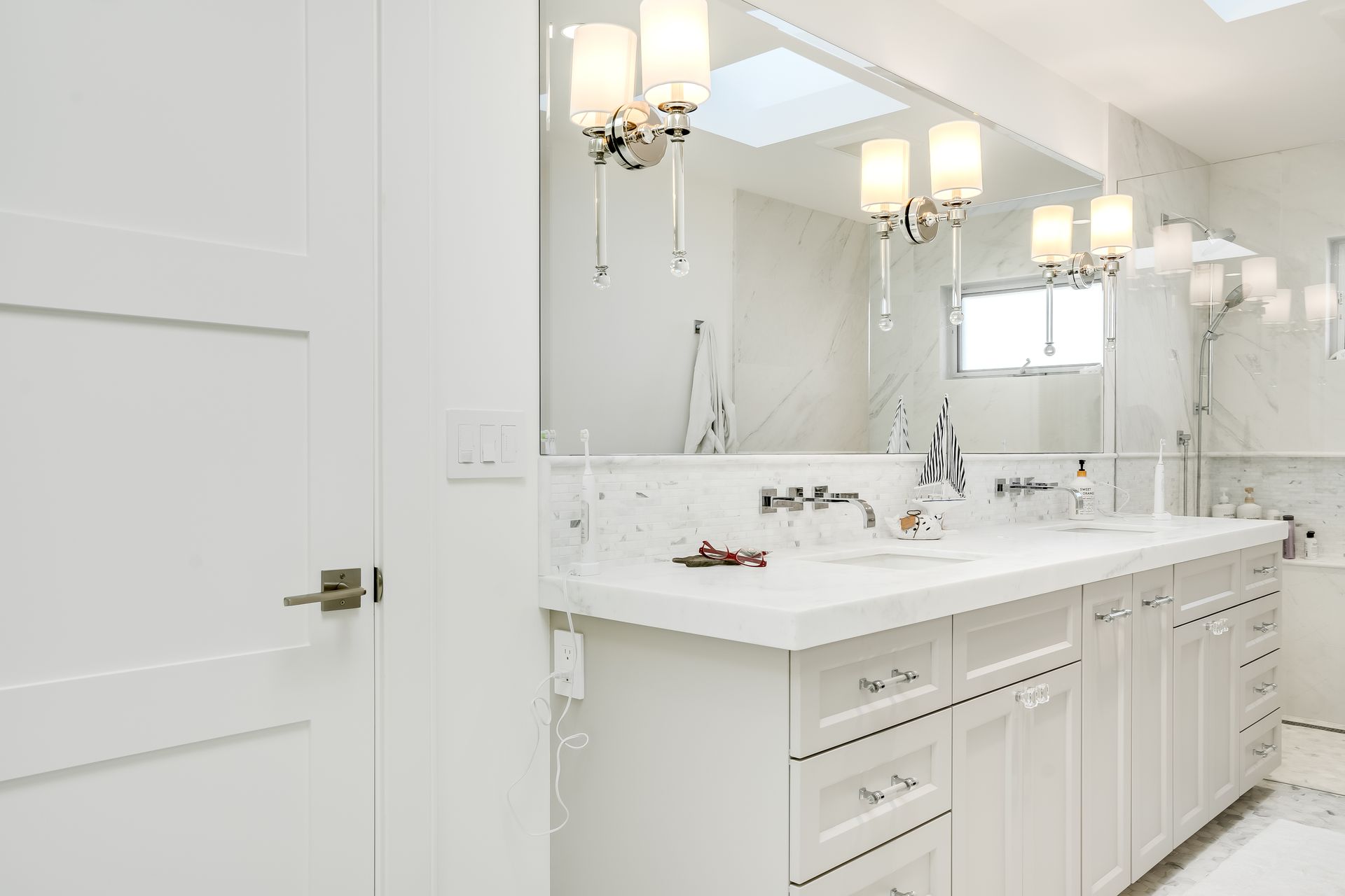 White bathroom with double vanity, large mirror, and overhead lighting.
