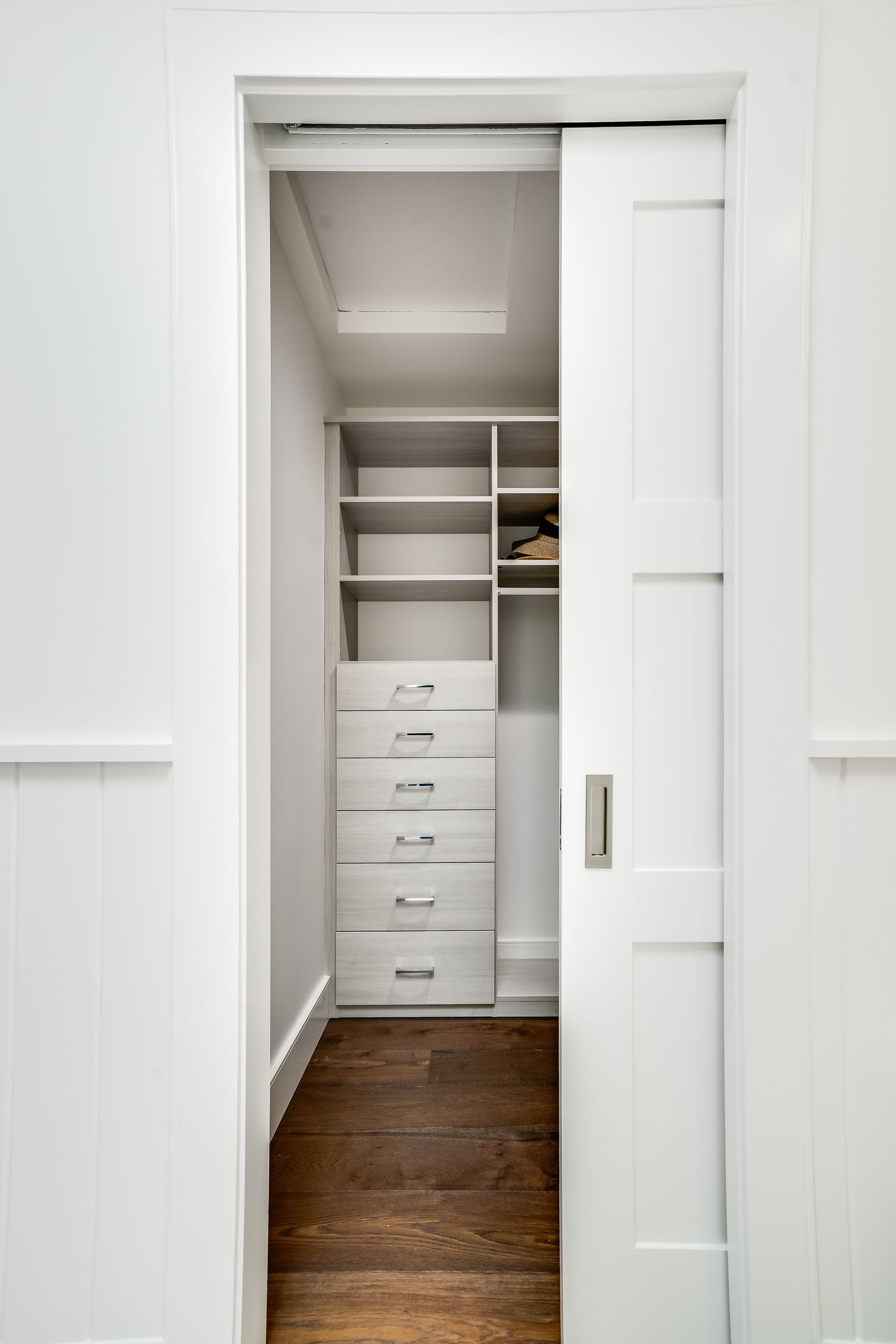 White closet with sliding door slightly open, revealing wooden floor and shelving.