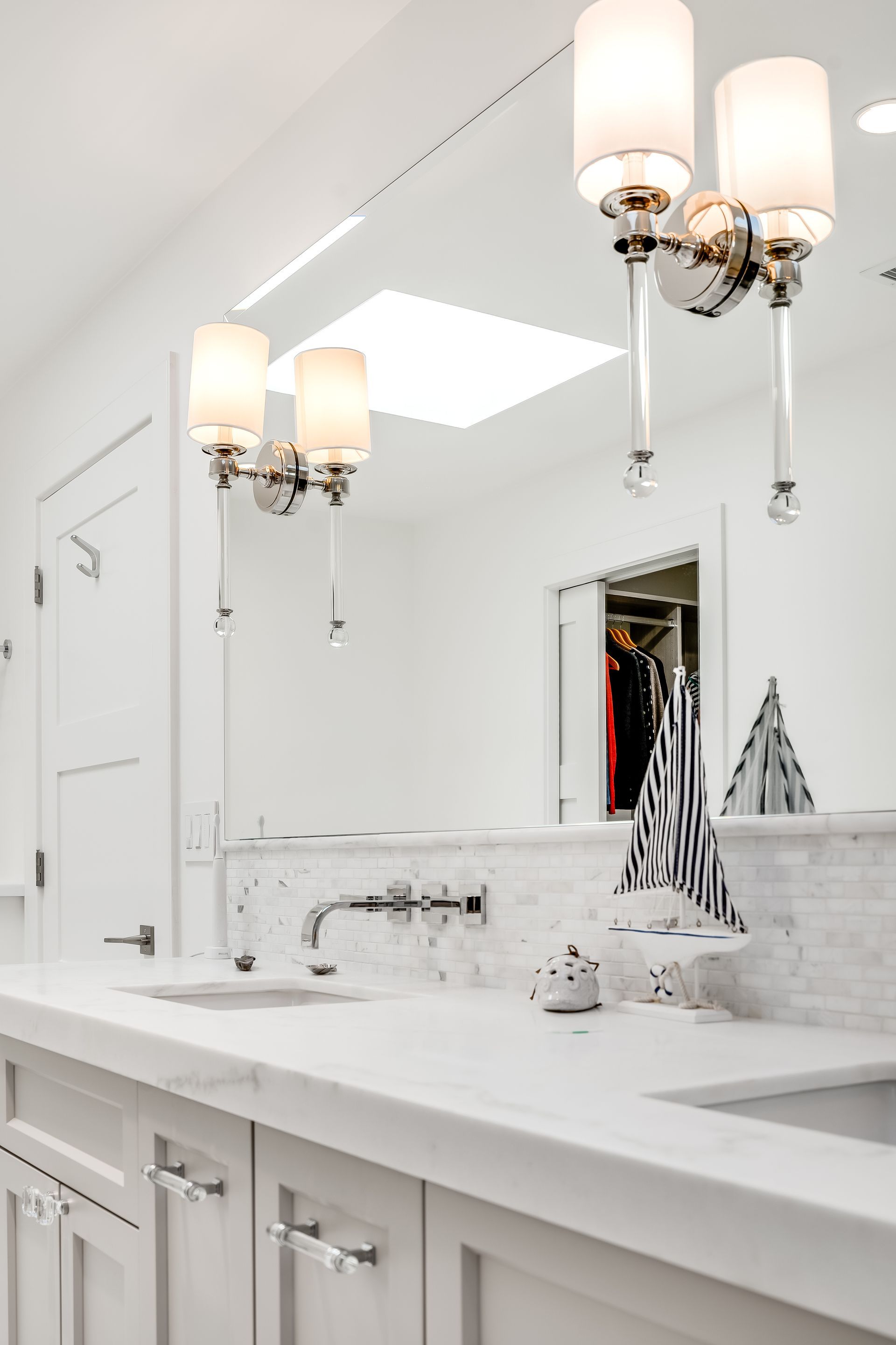 White bathroom with a large mirror, lights, and a white countertop with marble tiles.