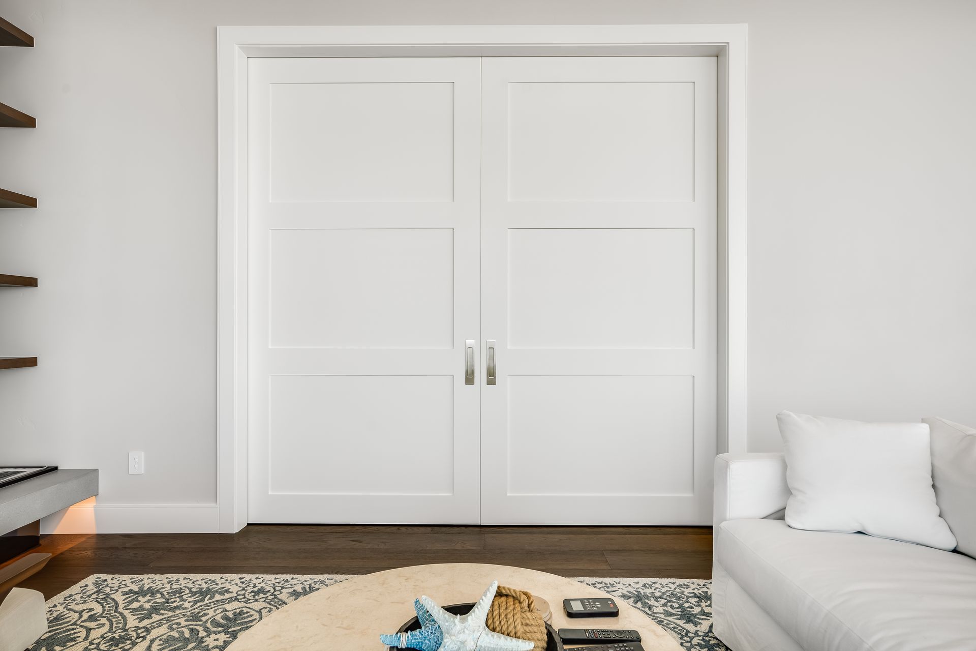 White double doors with silver handles in a minimalist living room setting.