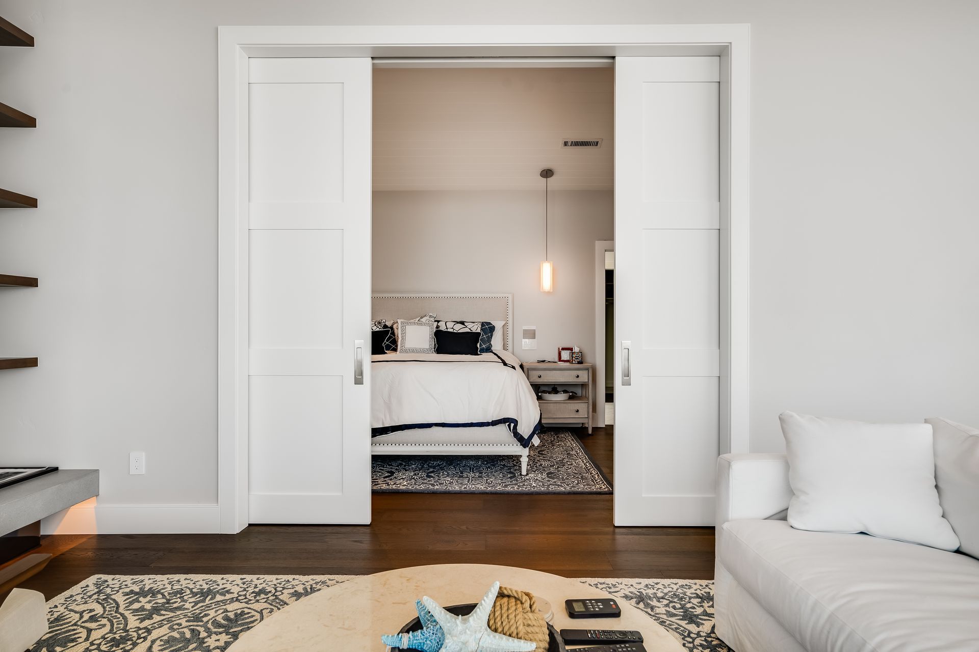White sliding doors open to a bedroom with a bed, nightstand, and rug.