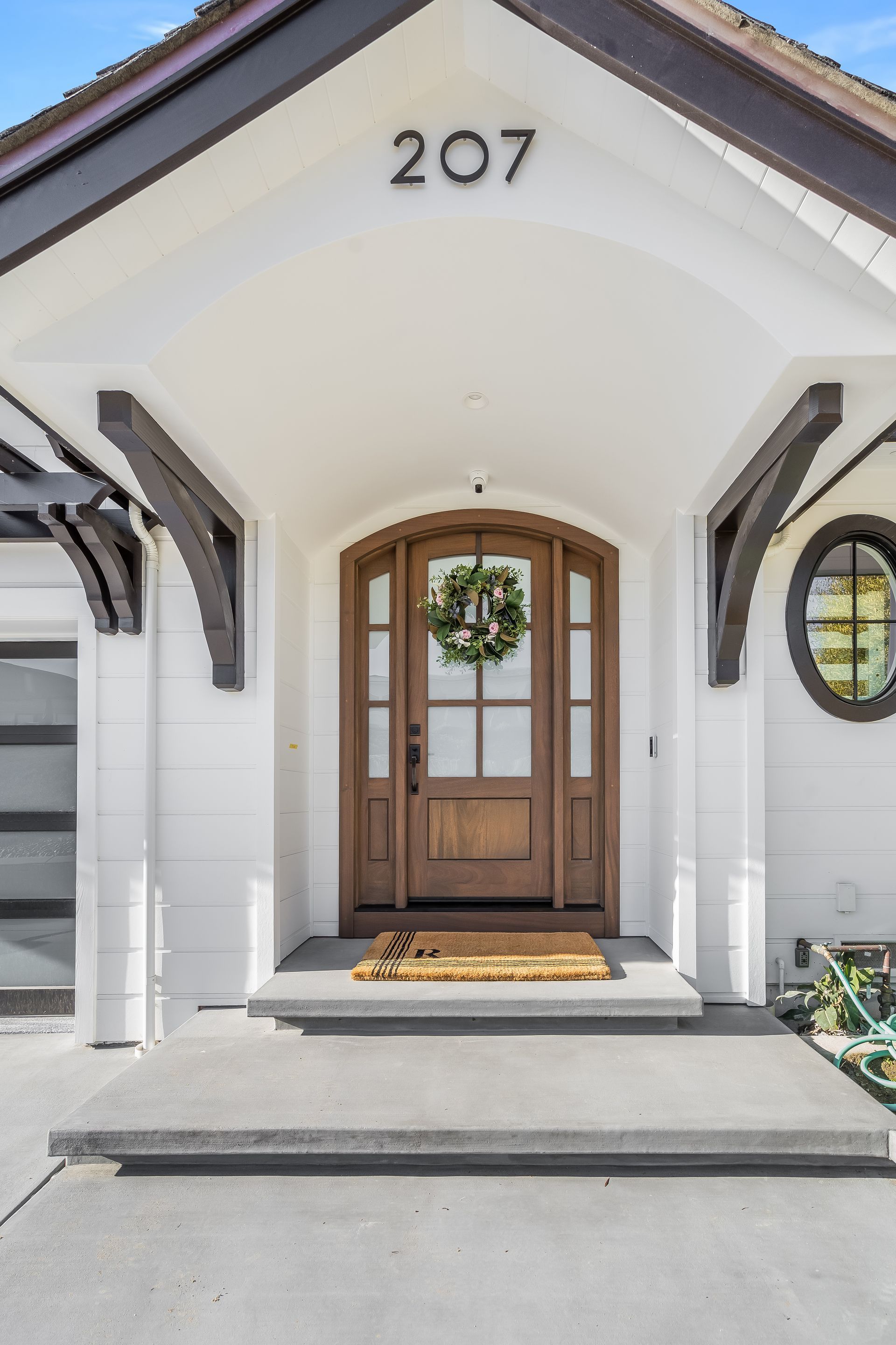 Front entrance of a white house with a wooden door and a wreath, address 207 above.