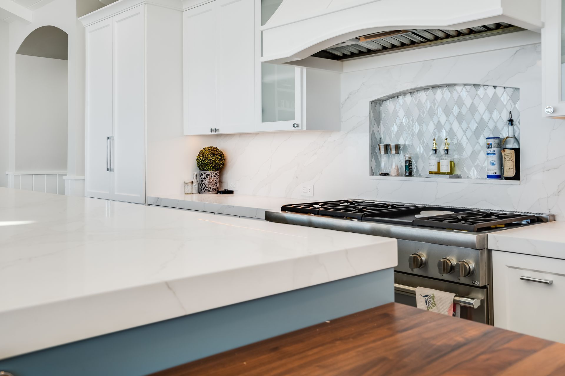 White kitchen with countertop, stove, and built-in shelving. Blue and wood accents.
