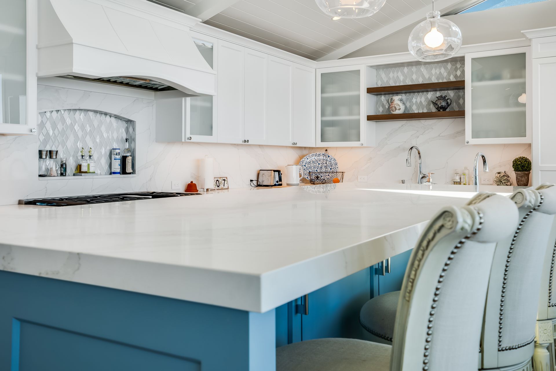 White kitchen with blue island and white countertops. Two upholstered chairs at the island.
