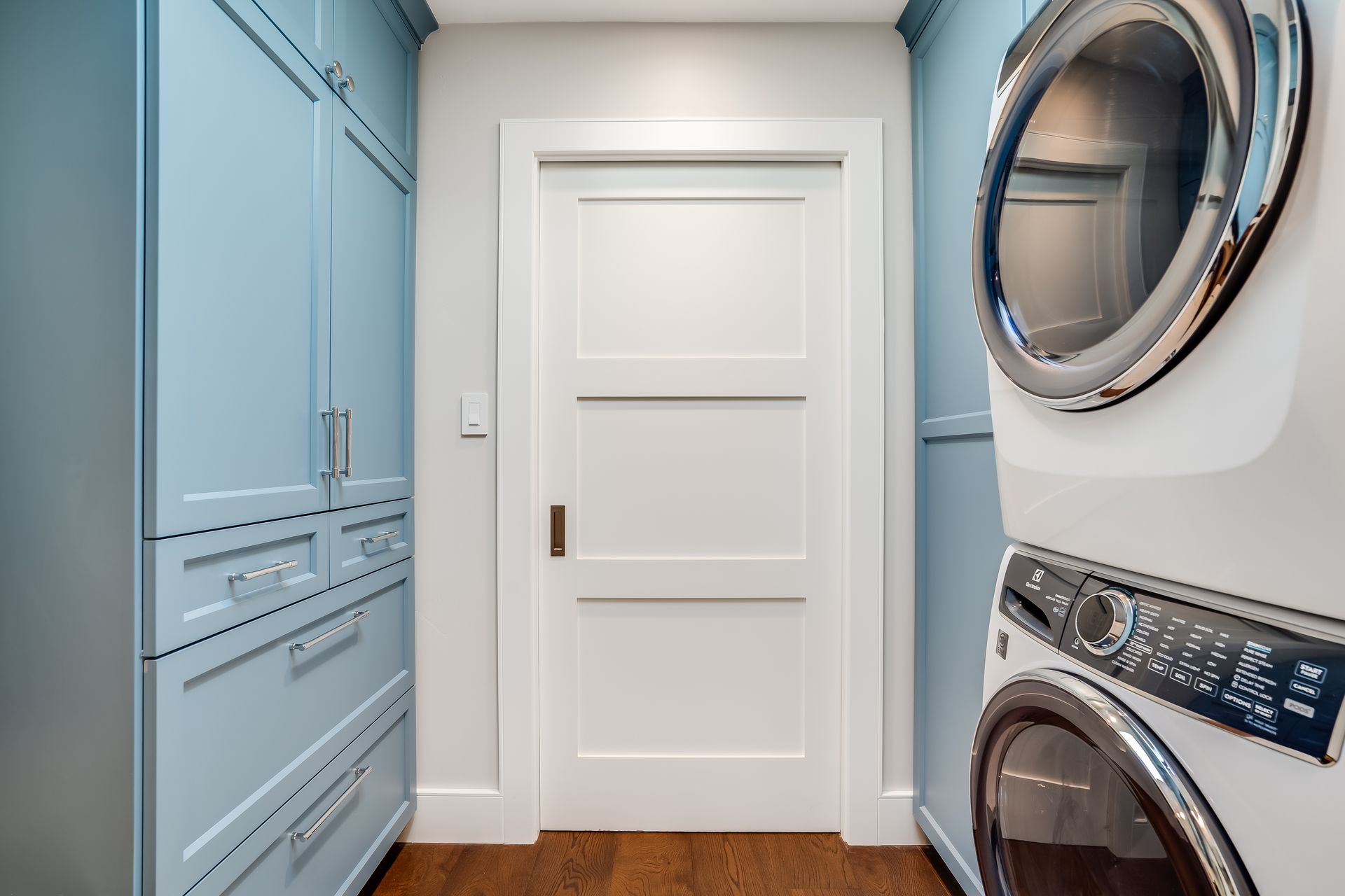Laundry room with blue cabinets, white door, and stacked washer/dryer.