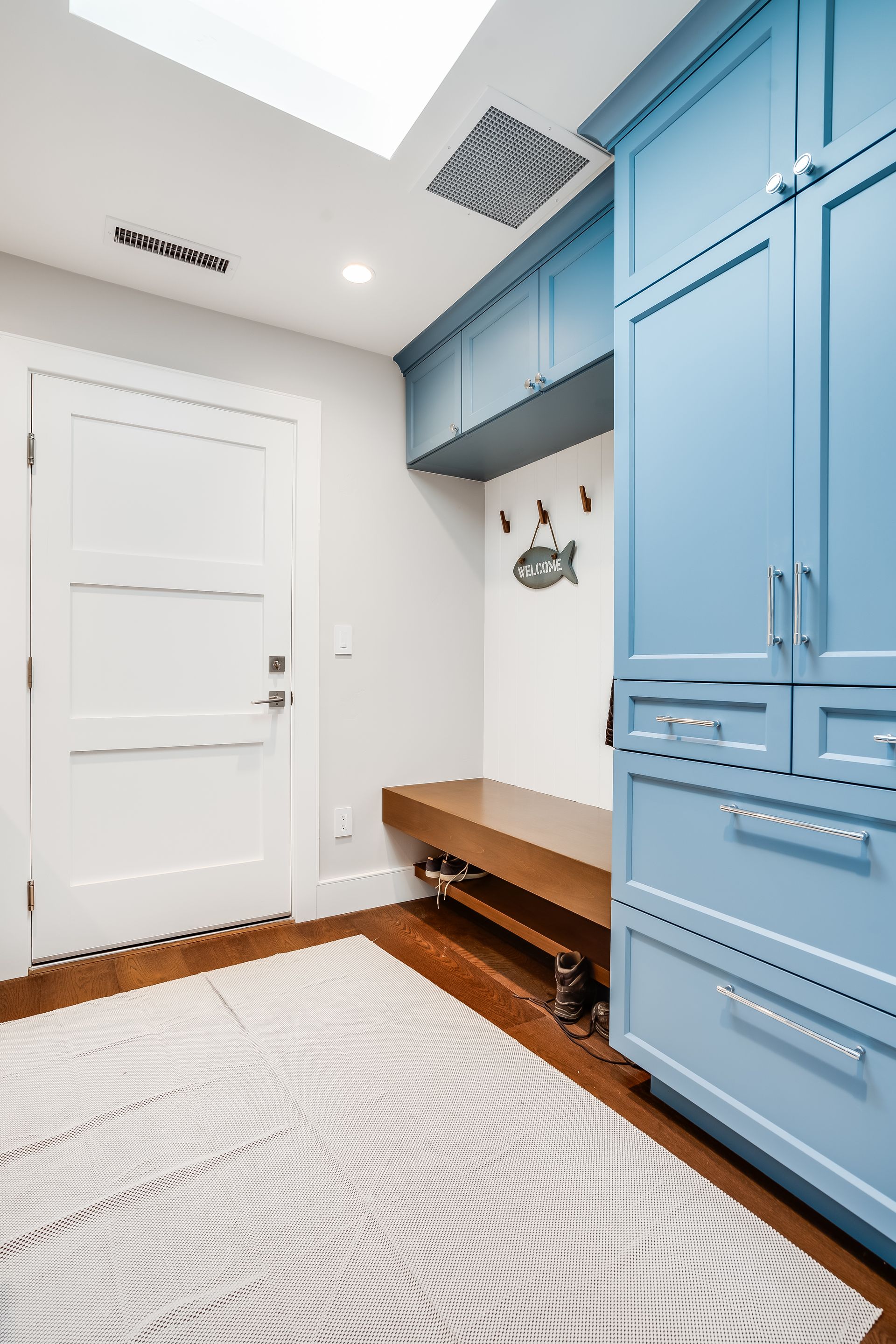 Entryway with a blue cabinet, wooden bench, white door, and patterned rug.