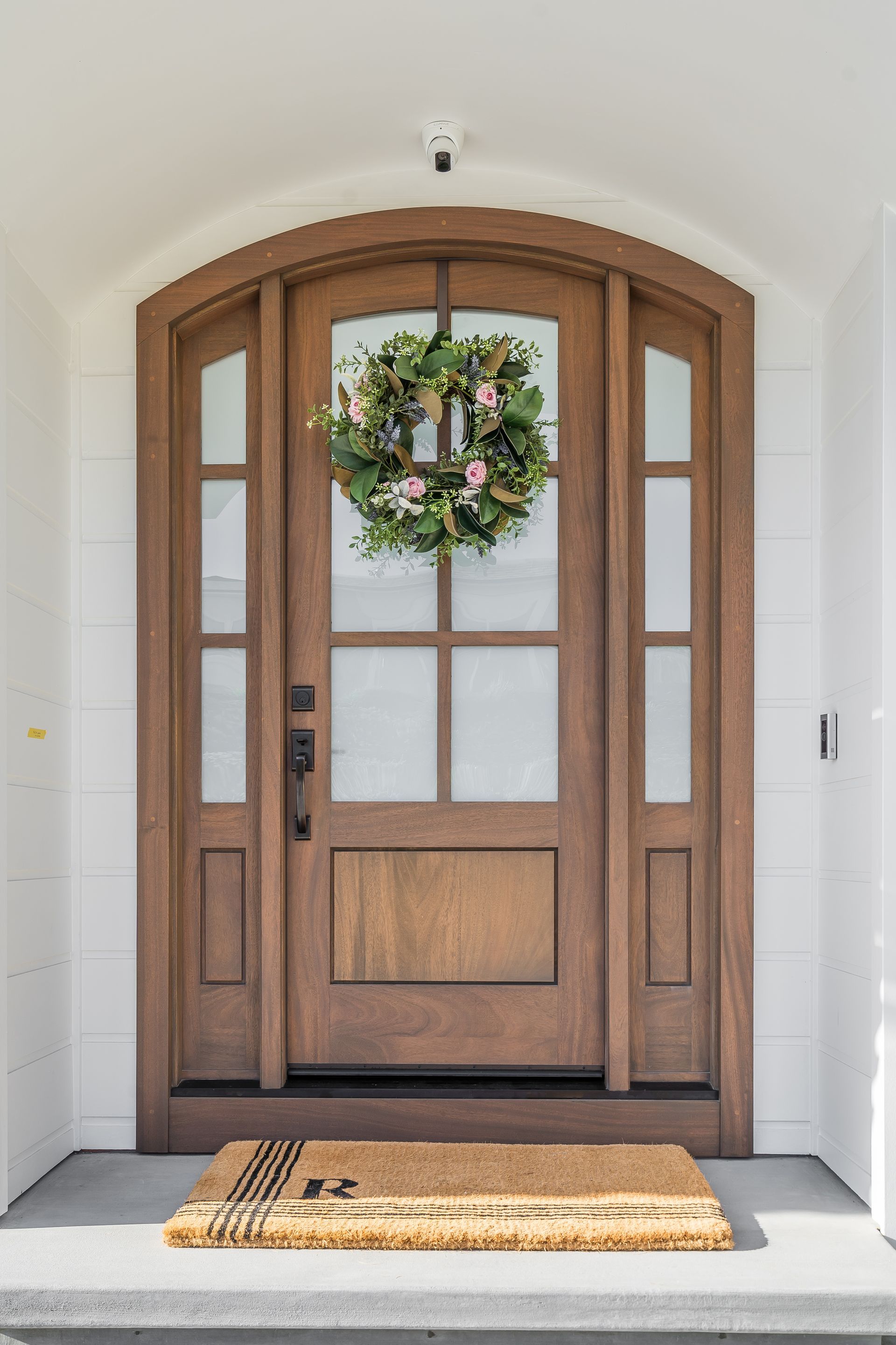 Wooden front door with sidelights and a floral wreath; a doormat sits on the step.