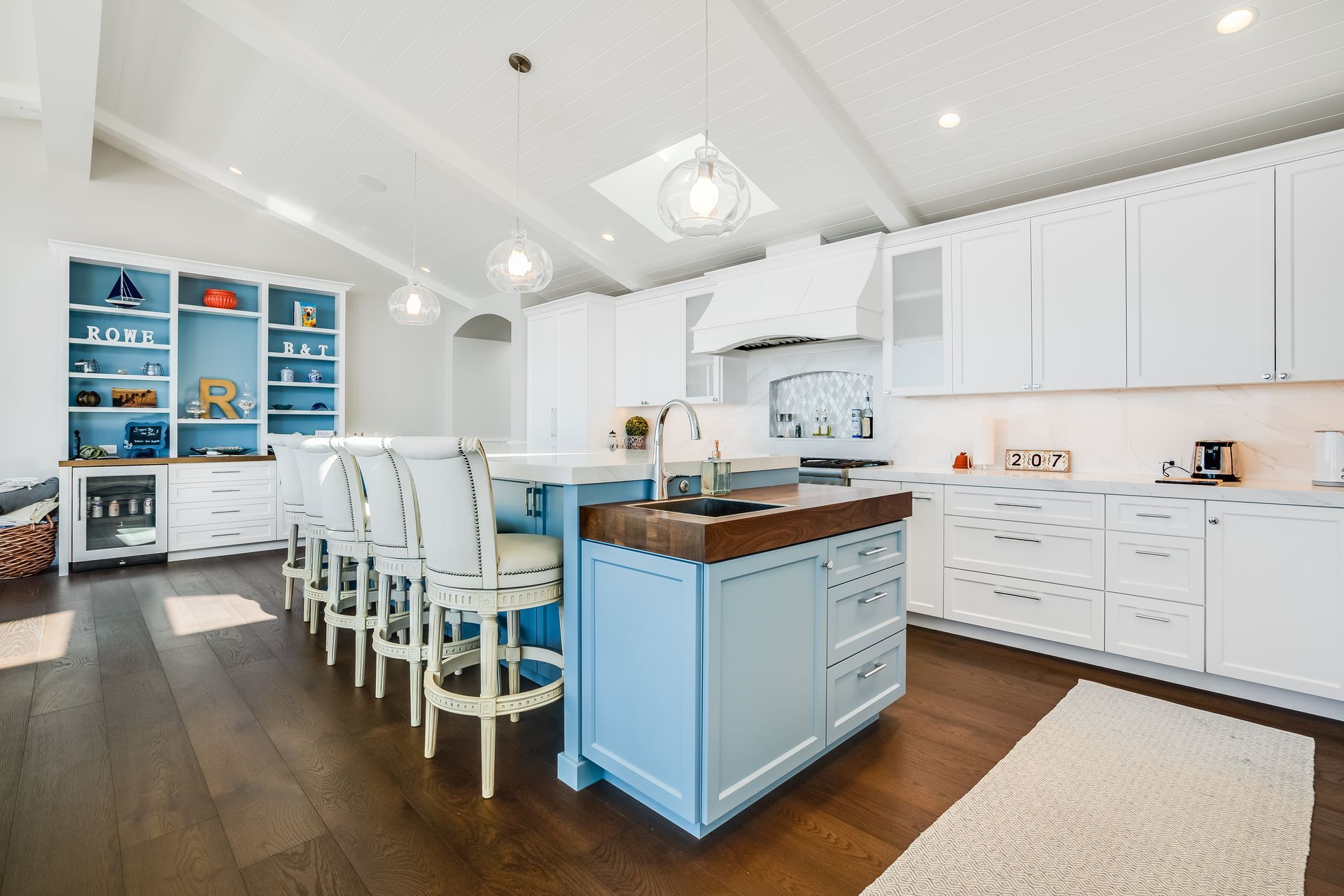 Blue and white kitchen with large island, wood floors, and white cabinets; coastal style.