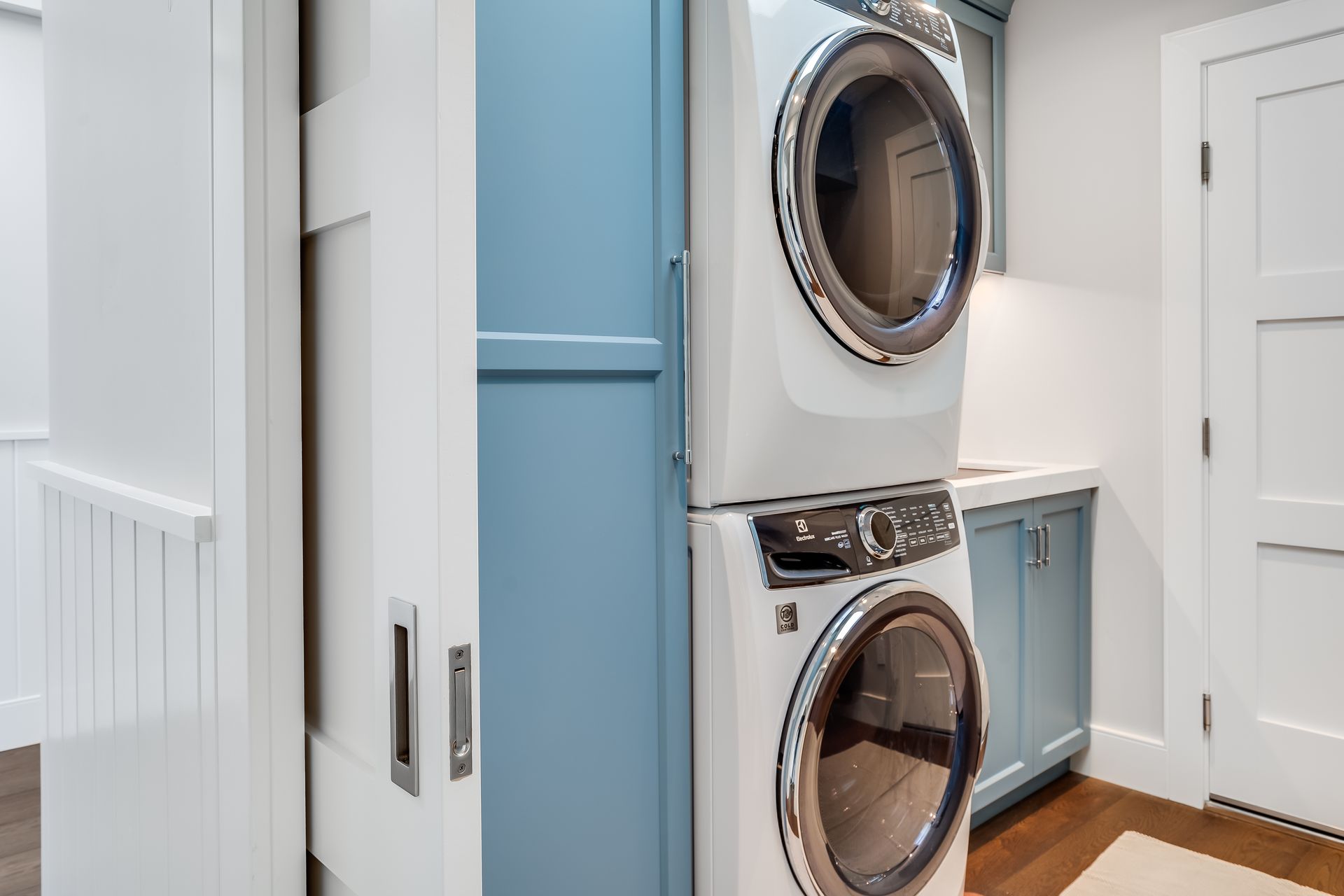 Stacked white washer and dryer in a laundry room with blue cabinets and sliding door.