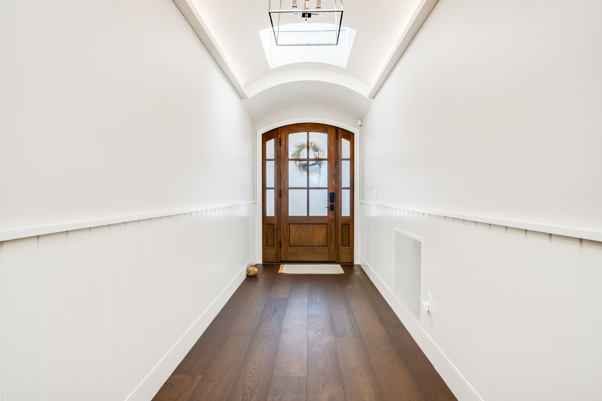 Hallway with white walls, wood floor, and a wooden door with glass panes at the end.