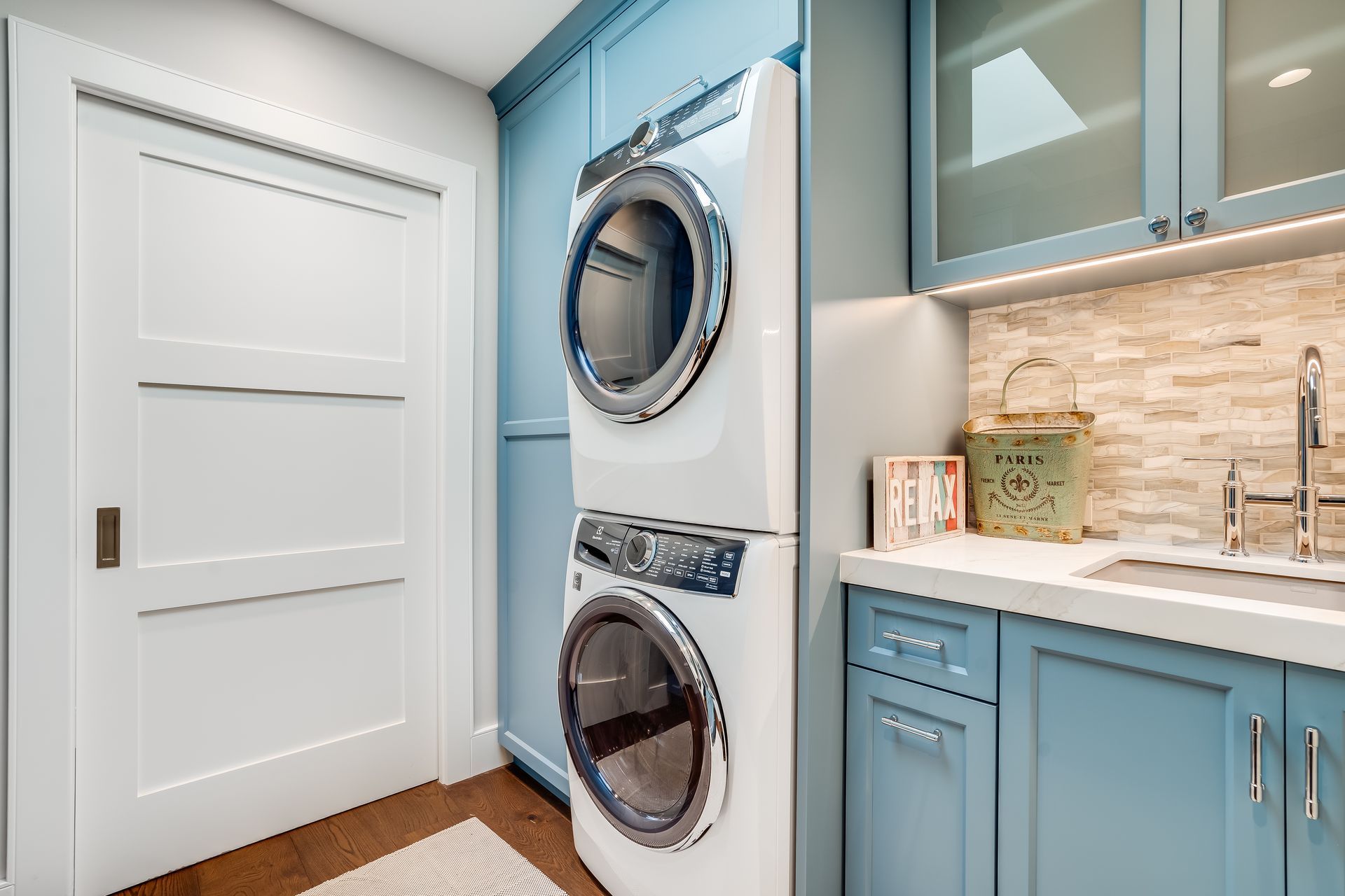 Laundry room with stacked blue washer/dryer, blue cabinets, sink, and white door.