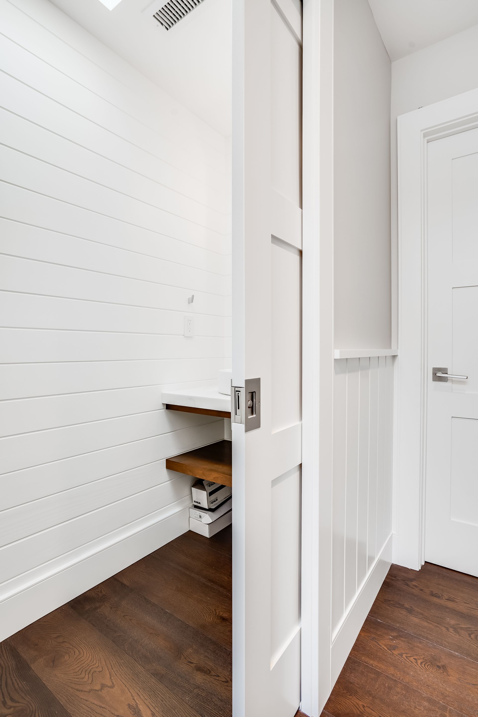 Open white door leading into a small, bright closet with wood shelving and dark wood floors.
