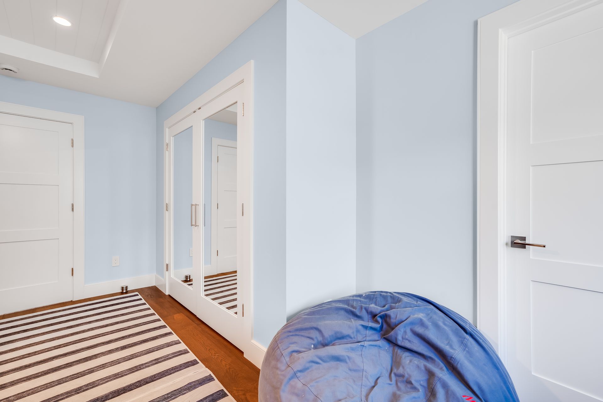 Hallway with blue walls, white doors, striped rug, mirrored closet, and a blue beanbag chair.