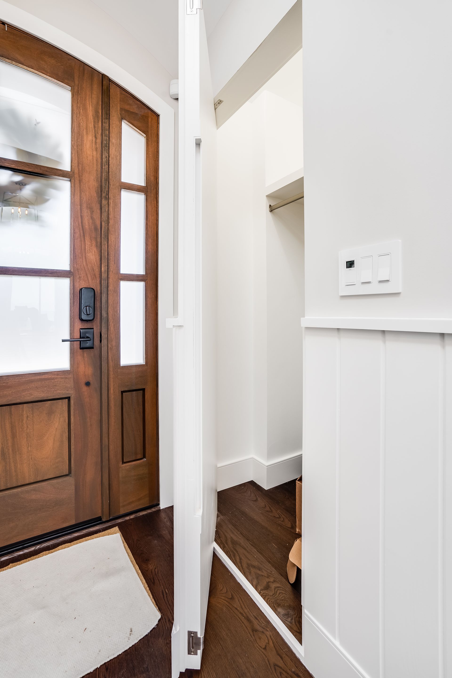 Wooden door with glass panels opens to a white hallway with stairs, light switch on wall.