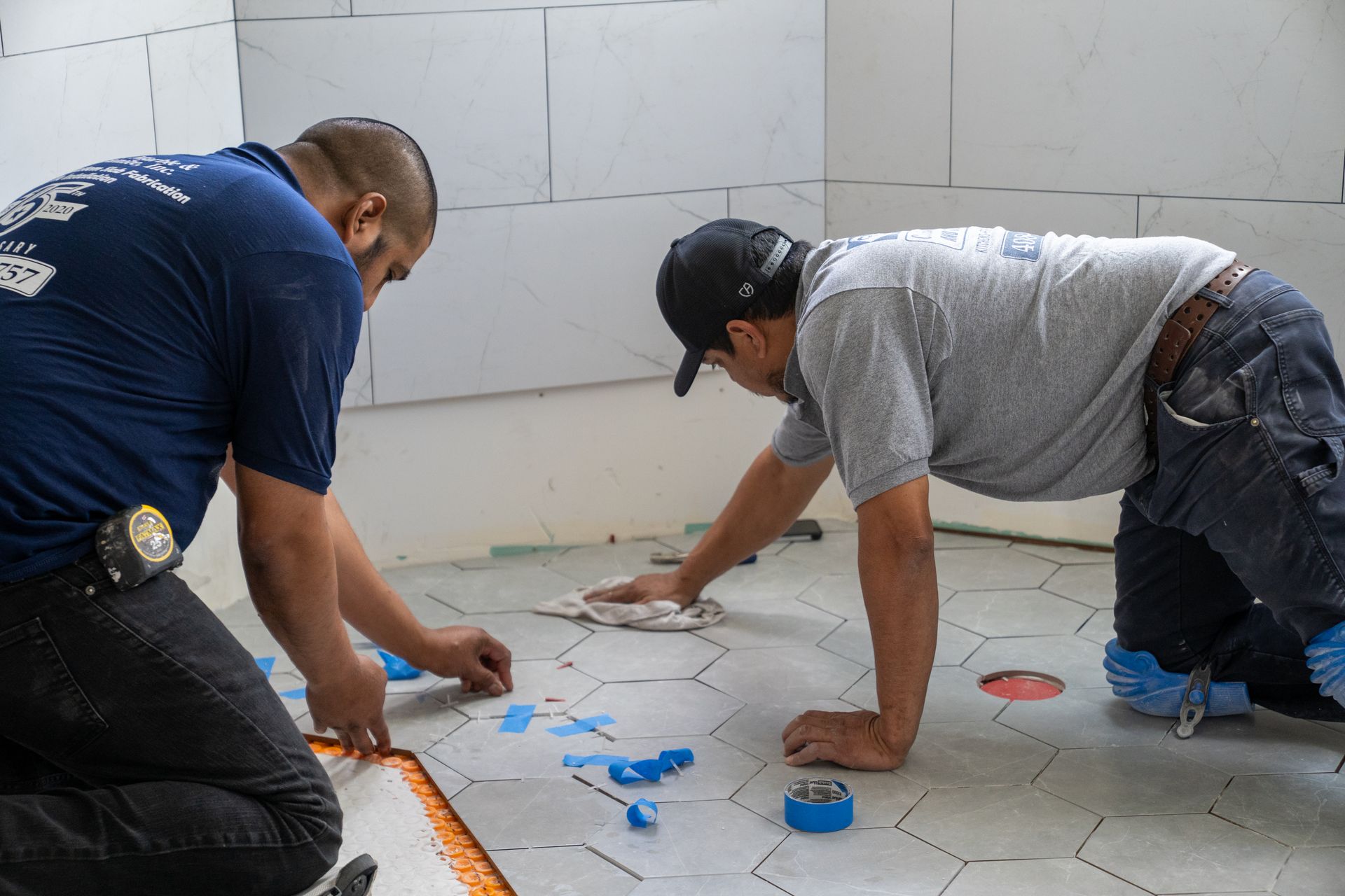 Two men install hexagonal floor tiles in a bathroom.