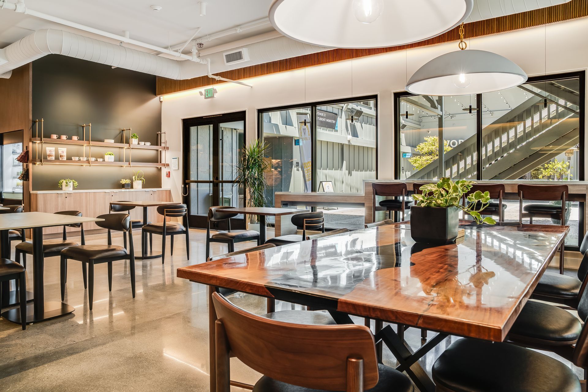 Modern cafe with tables and chairs, large windows, and decorative overhead lights.