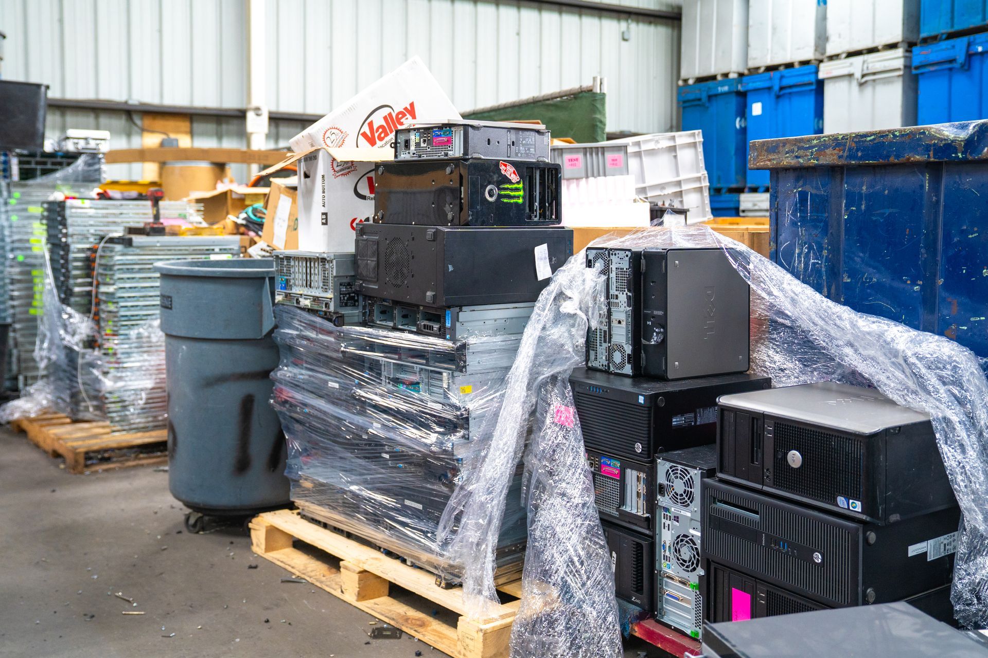 Computers and electronics stacked on pallets, wrapped in plastic, in a recycling facility.