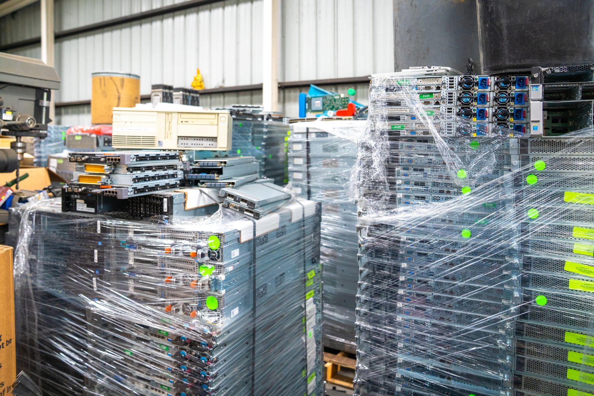 Stacks of server racks wrapped in plastic inside a warehouse; equipment for electronics recycling.