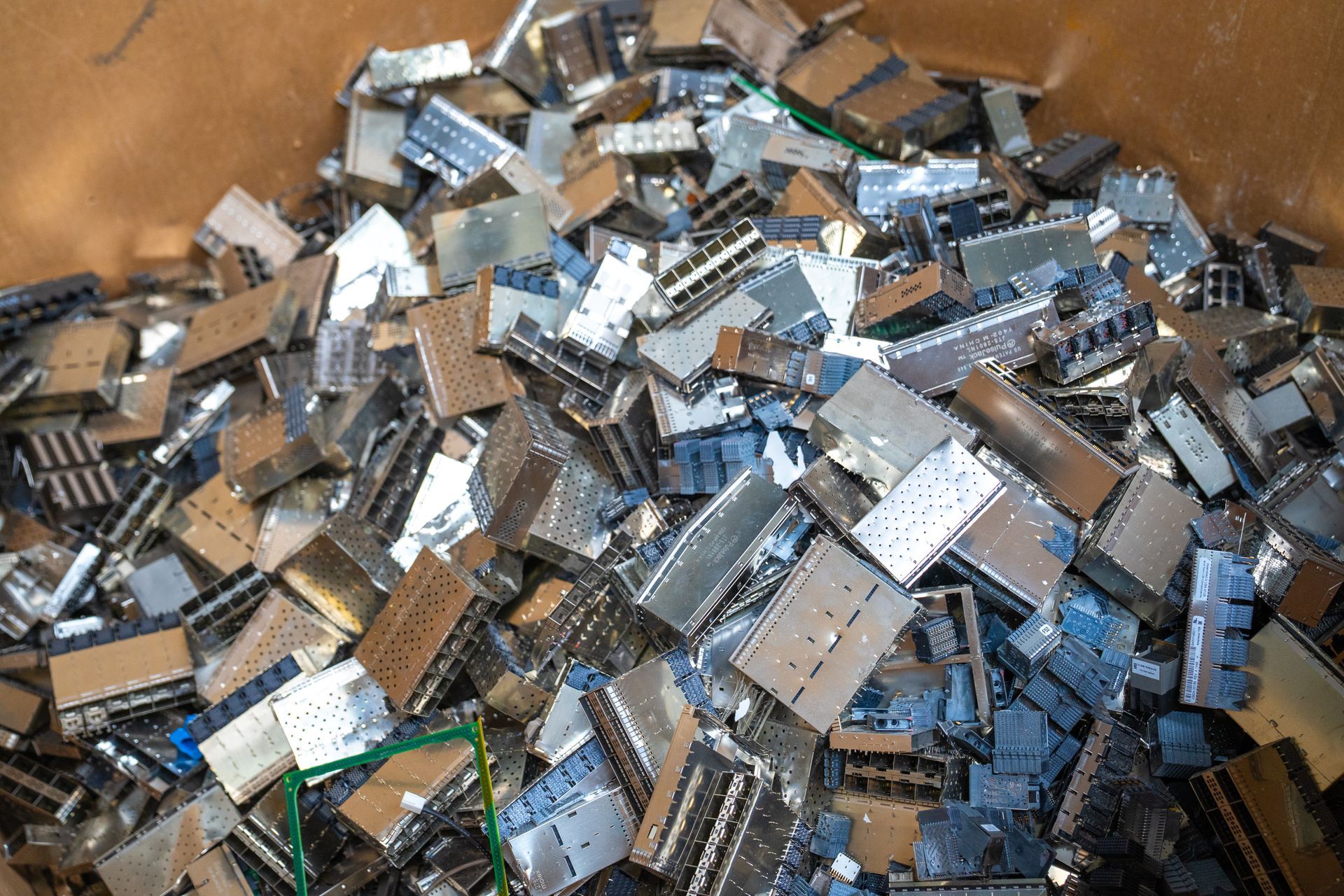 Pile of silver-colored metal computer components, likely for recycling, inside a cardboard box.