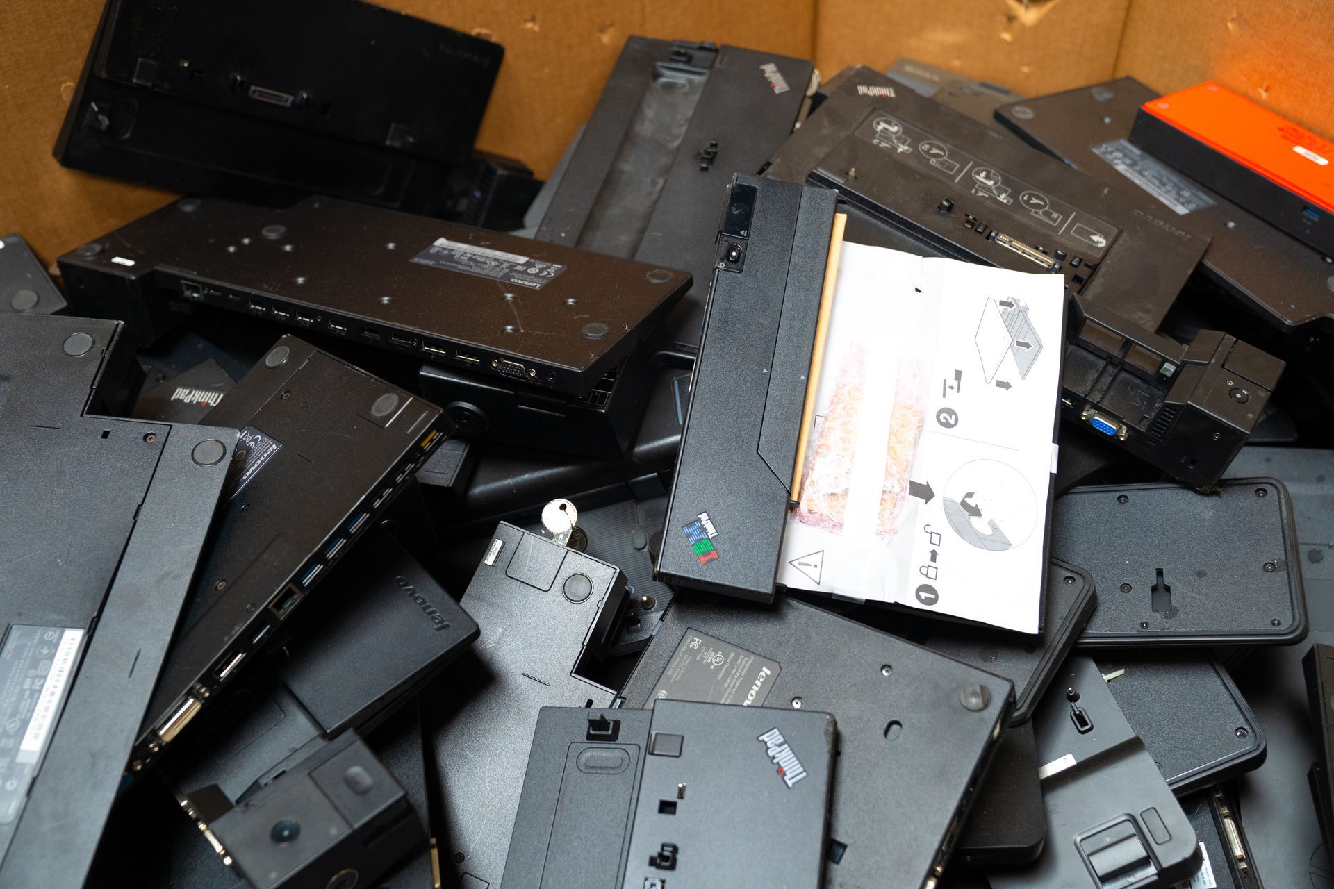 Pile of black laptop computer bases and cases in a box, possibly for recycling.