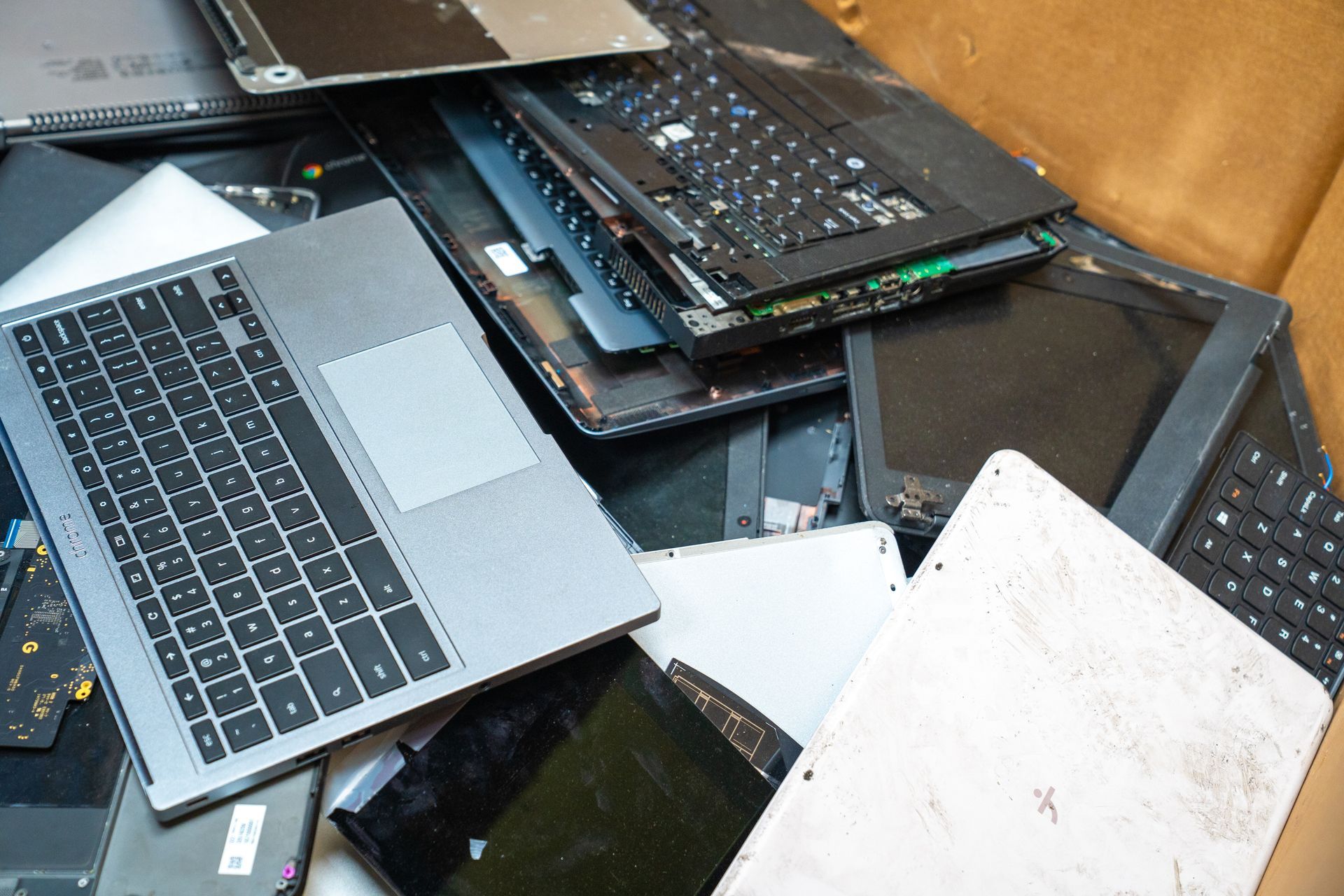Pile of discarded laptop parts in a box, including screens, keyboards, and internal components.
