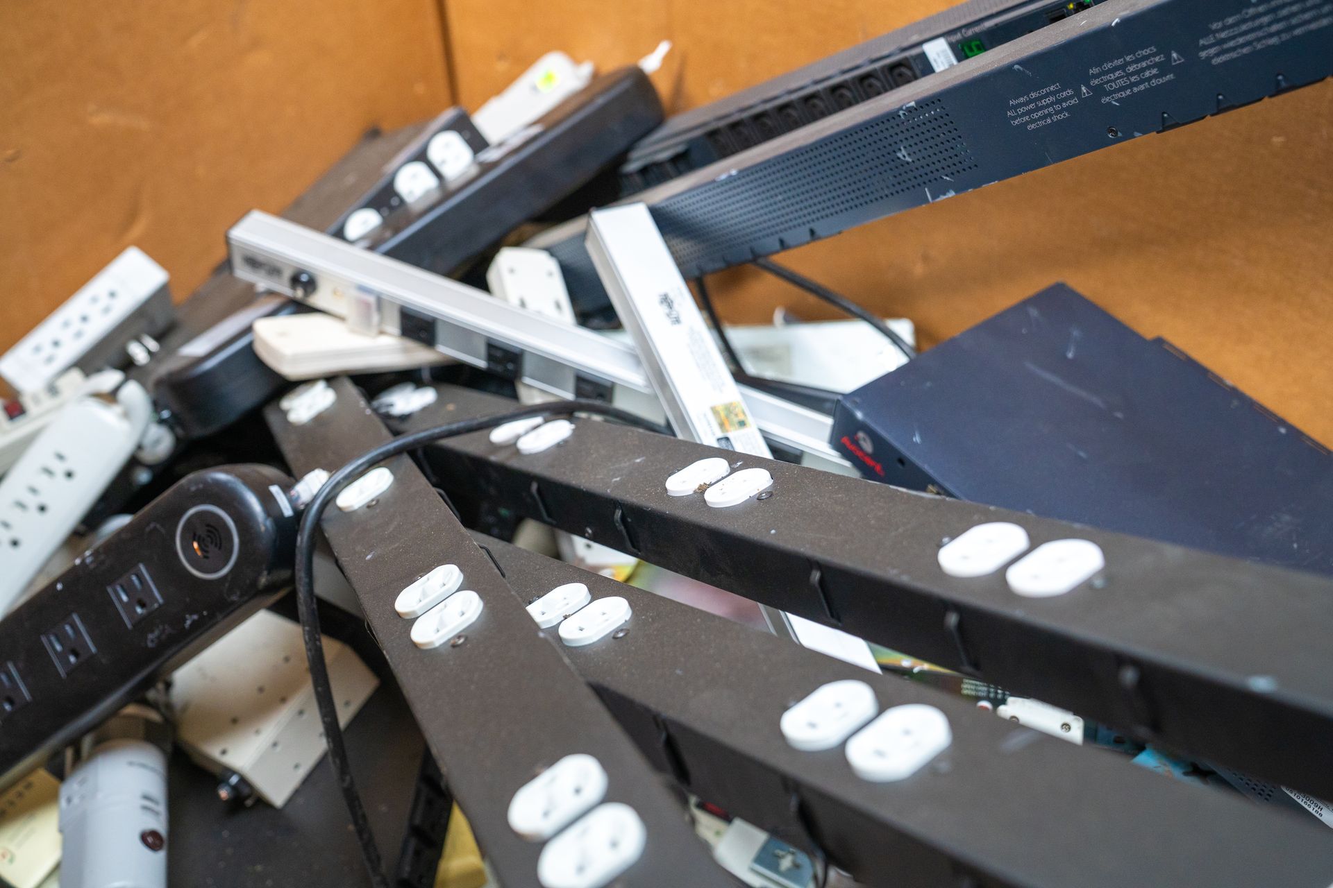 Pile of black and white power strips, cords, and electrical components in a bin.