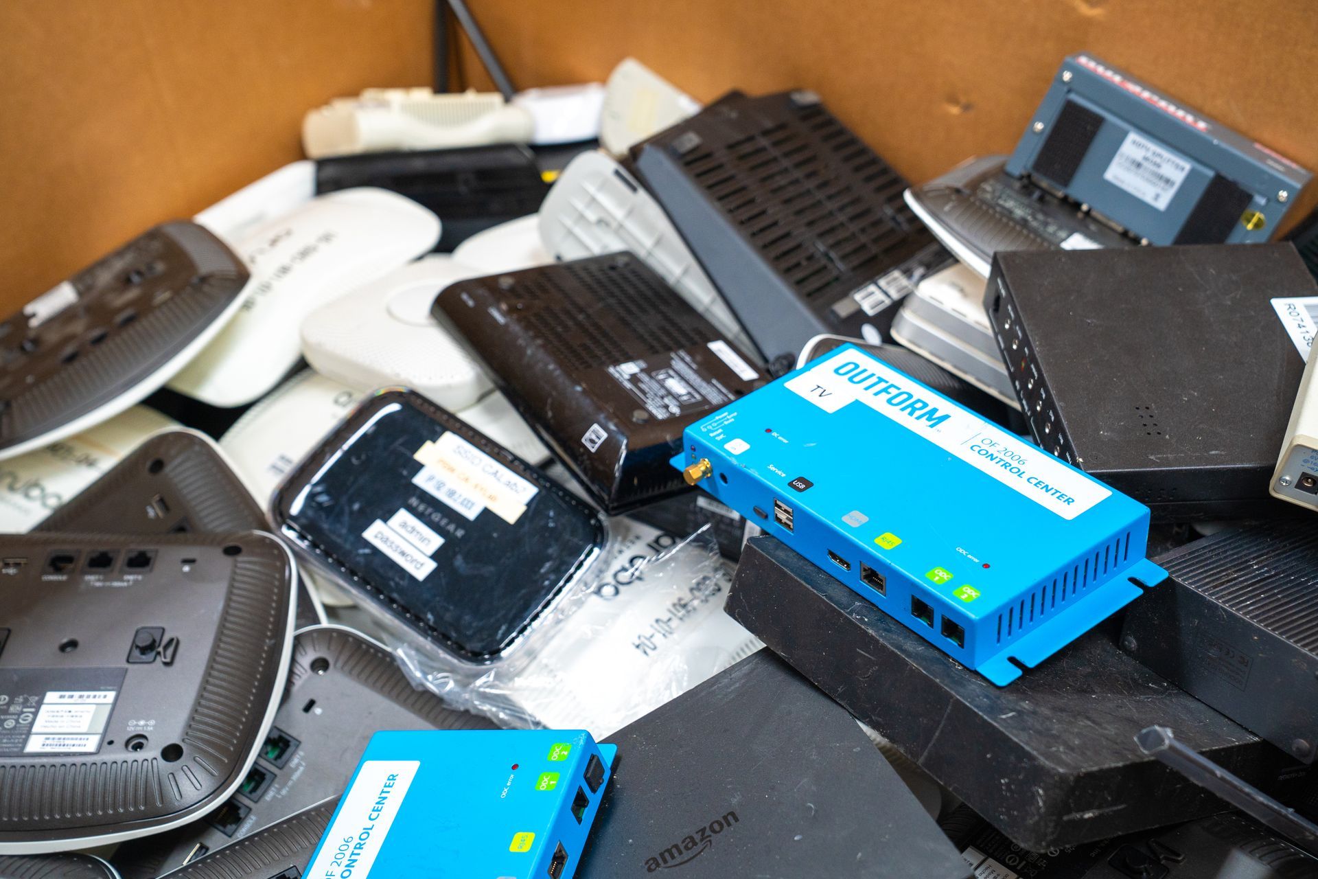 Box overflowing with various black, white, and blue electronic devices, likely routers and networking equipment.