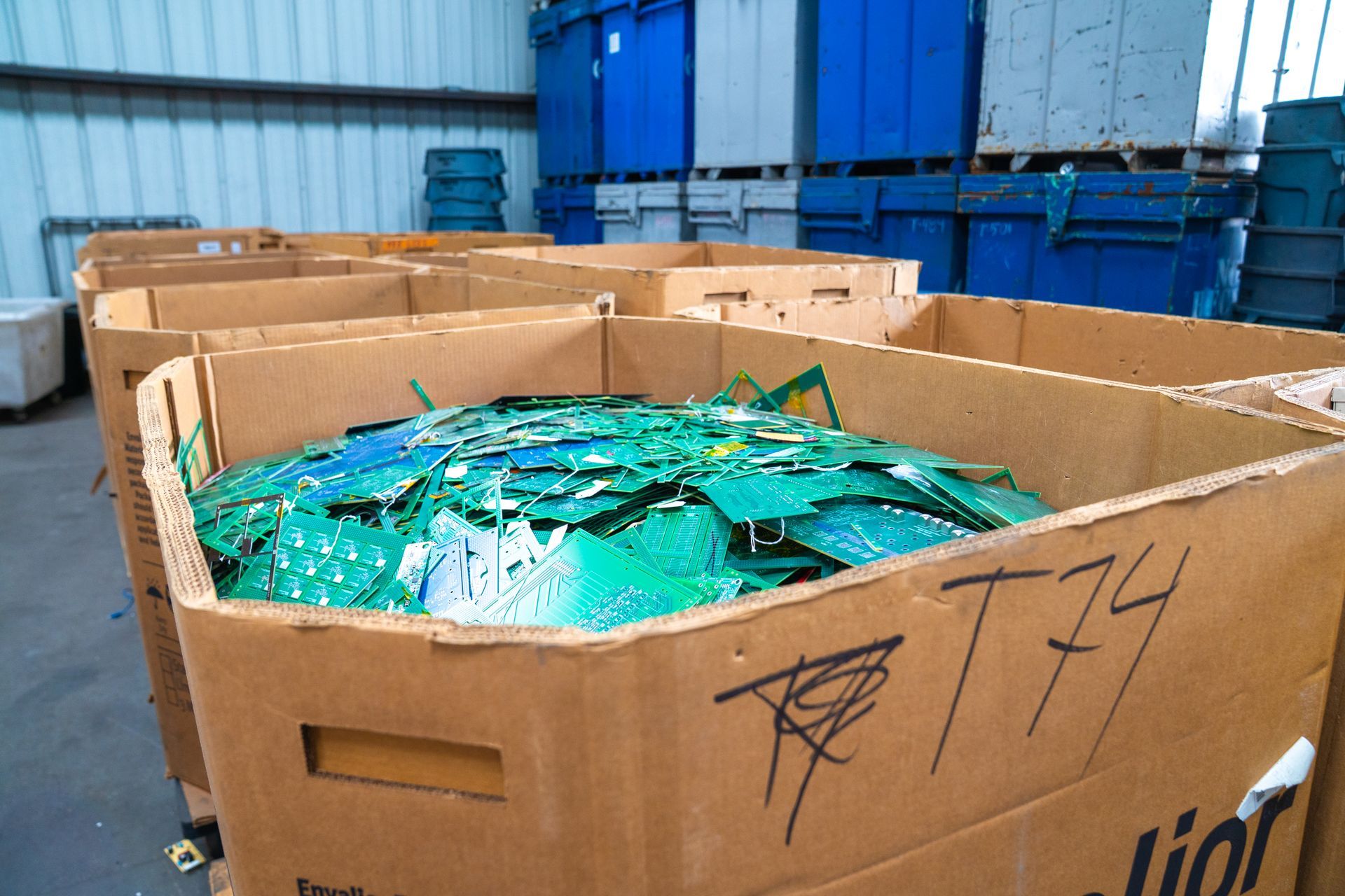 Cardboard boxes filled with shredded green and blue plastic, warehouse setting.