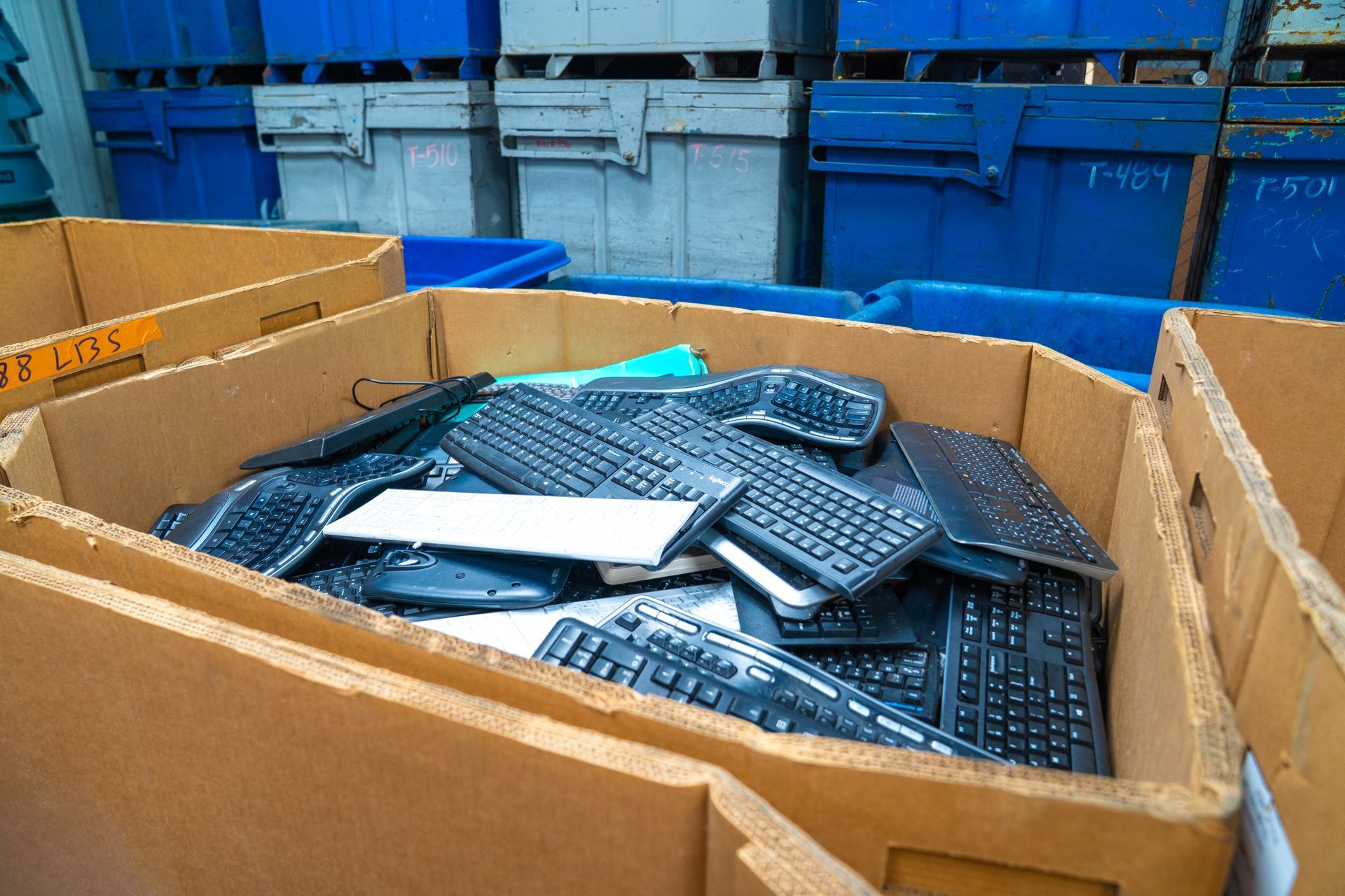 Cardboard box filled with black computer keyboards, ready for recycling.