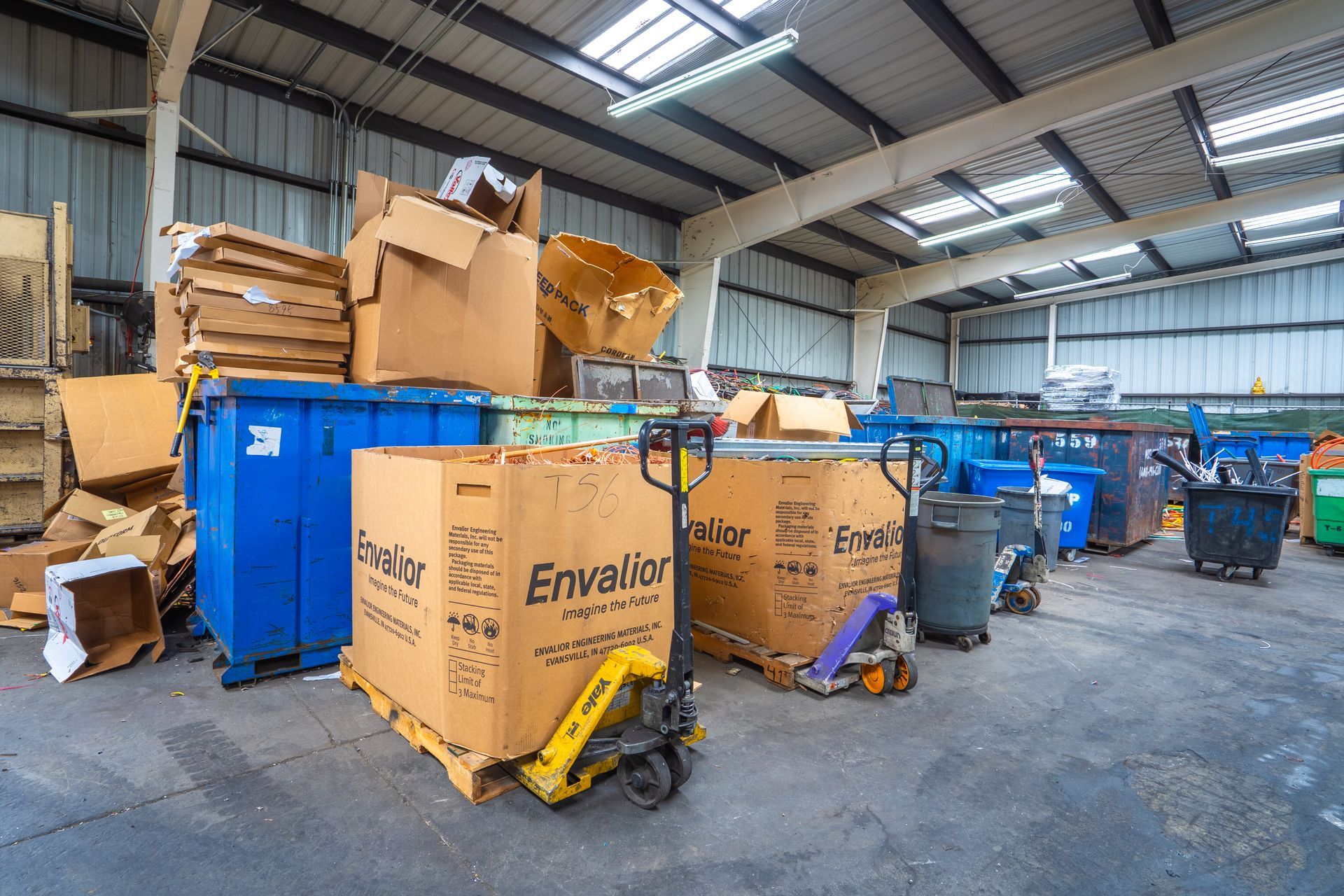 Cardboard boxes and bins in a recycling facility, a pallet jack stands ready to move the materials.