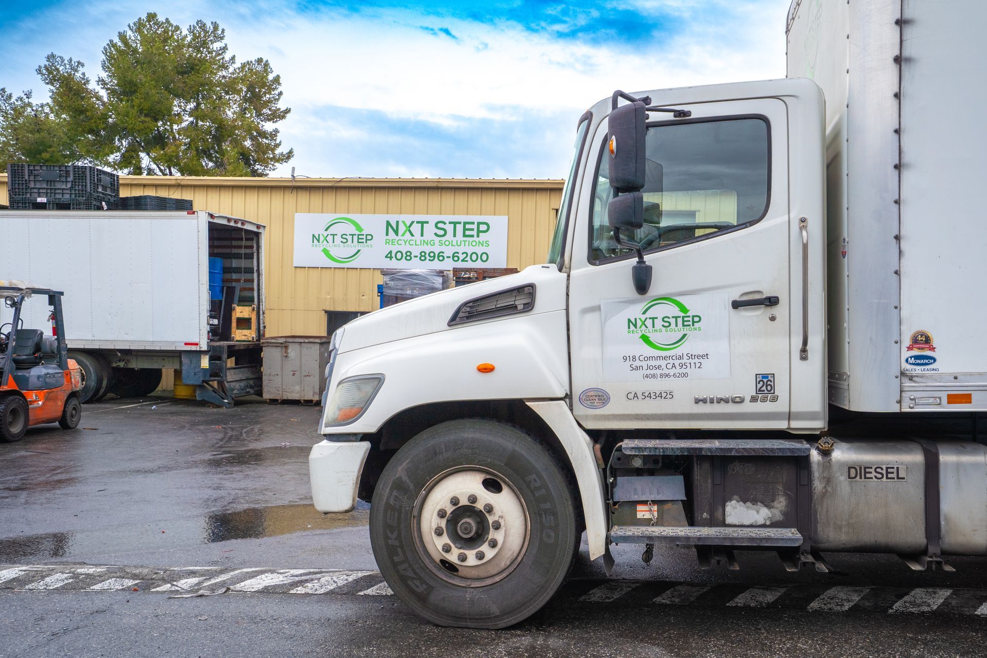 White Next Step truck parked at a loading dock; a forklift is nearby.
