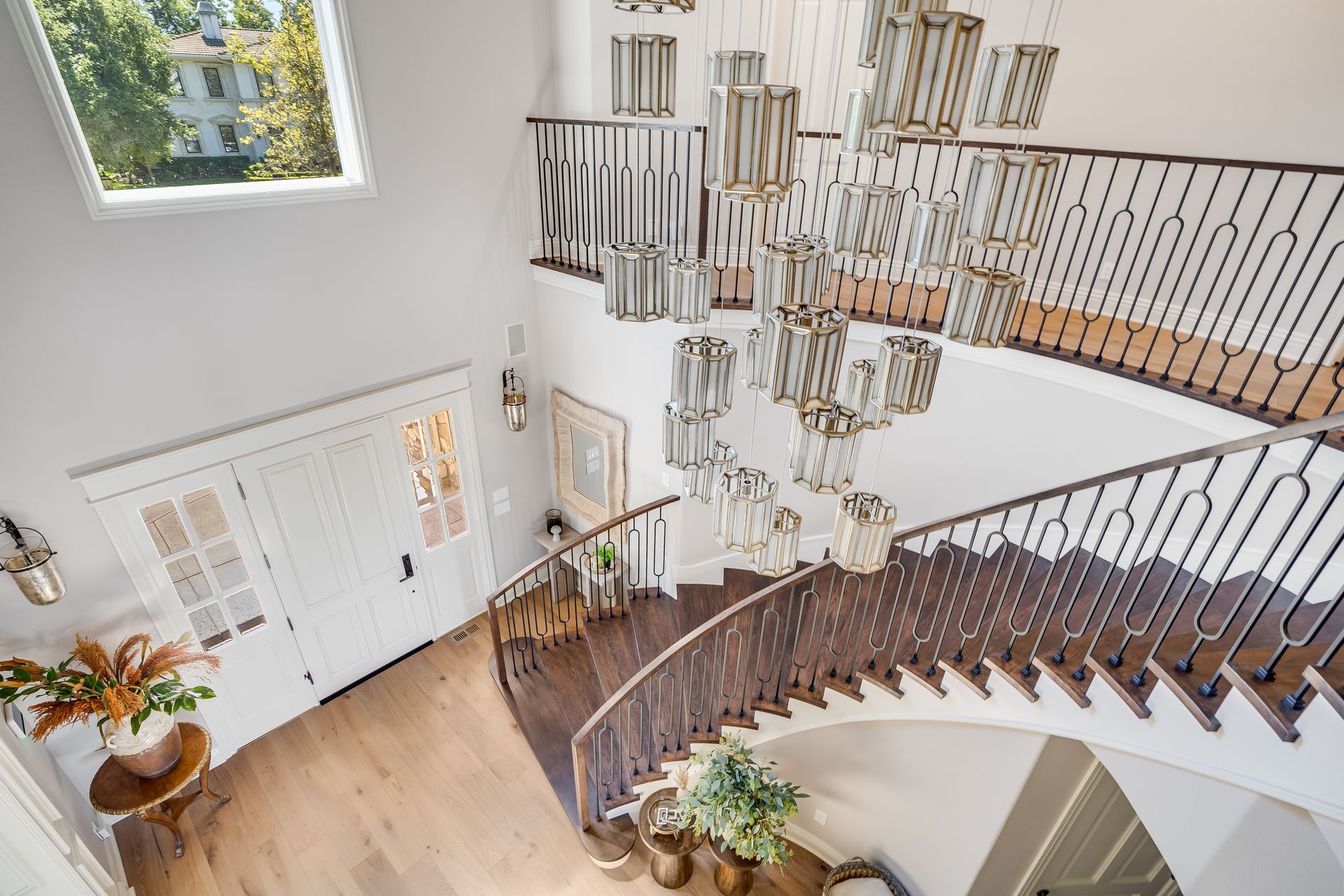 Grand foyer with curved staircase, crystal chandelier, white walls, and a glimpse of the outdoors.