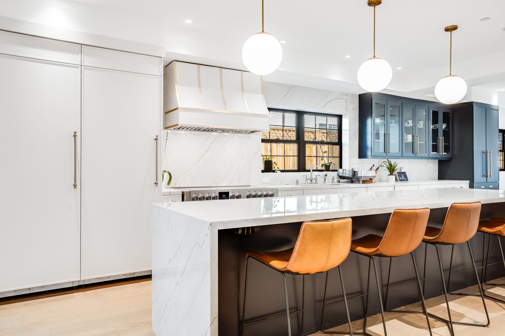 Modern kitchen with white cabinets, island with brown stools, and globe pendant lights.