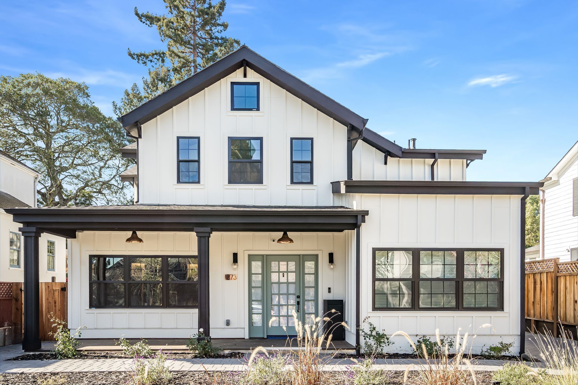 White farmhouse with black trim and a porch, under a blue sky.