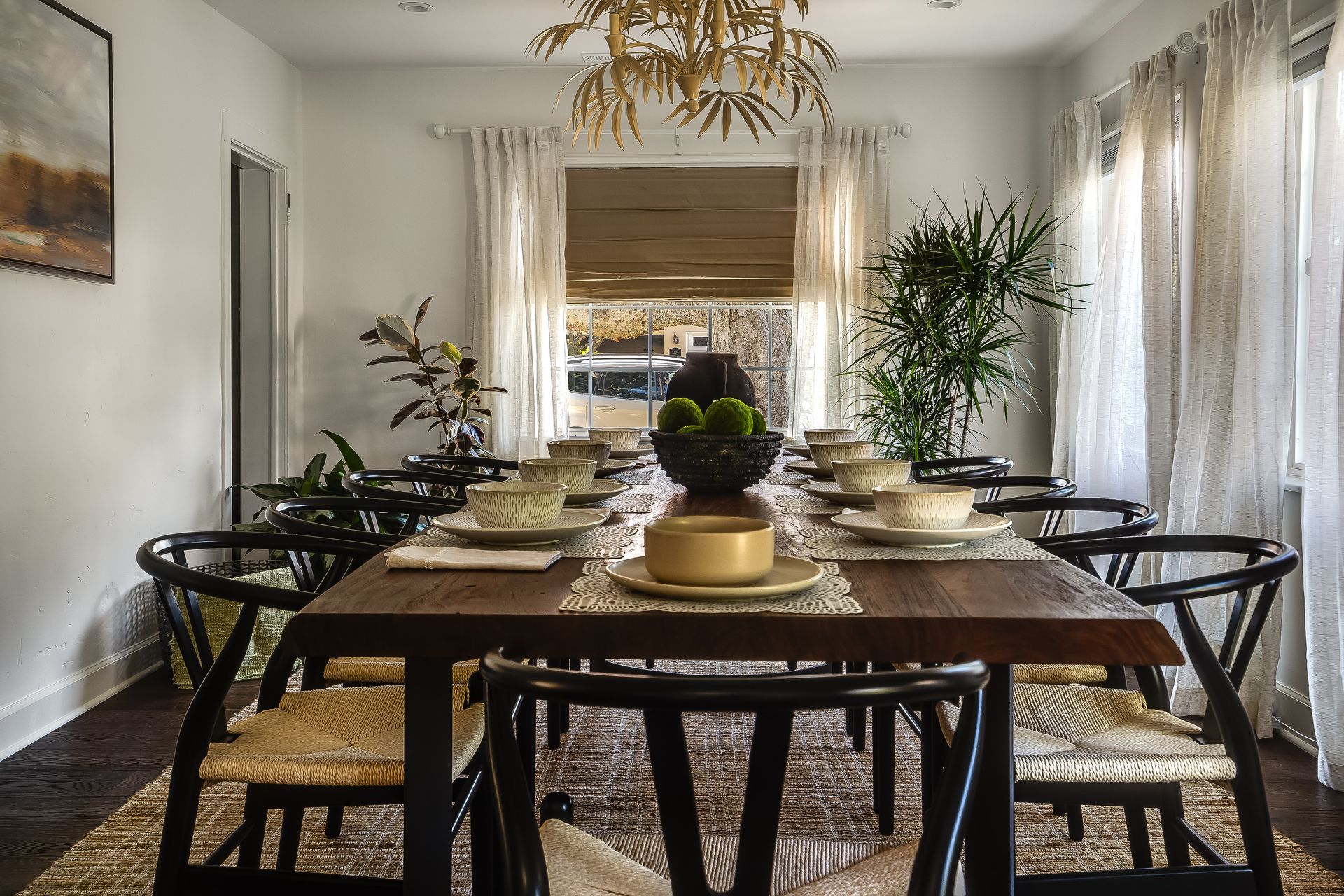 Dining room with wooden table, black chairs, cream curtains, and centerpieces.