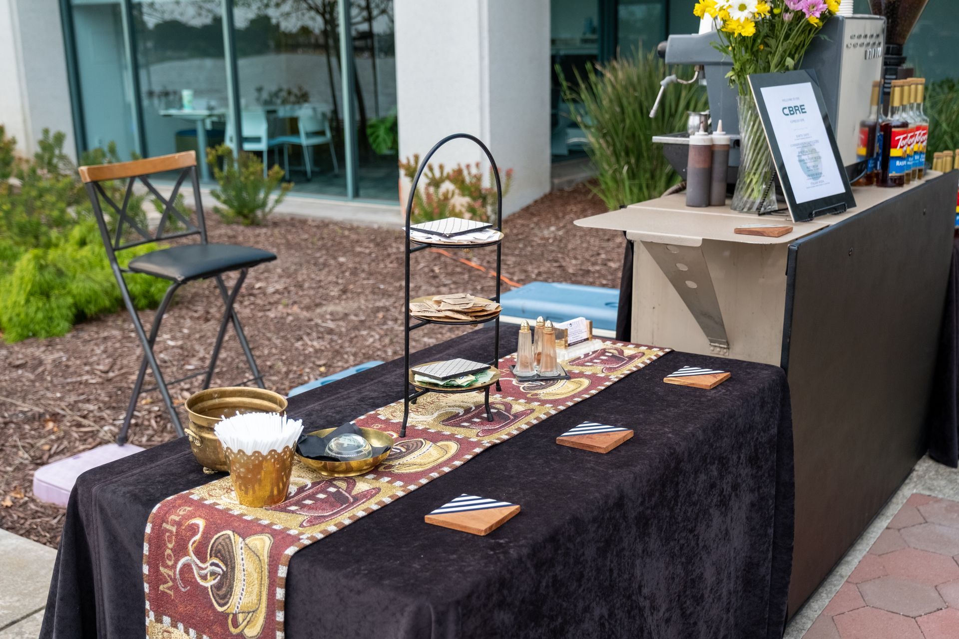 Coffee station setup with snacks, flowers, and a chair. Outdoor setting.