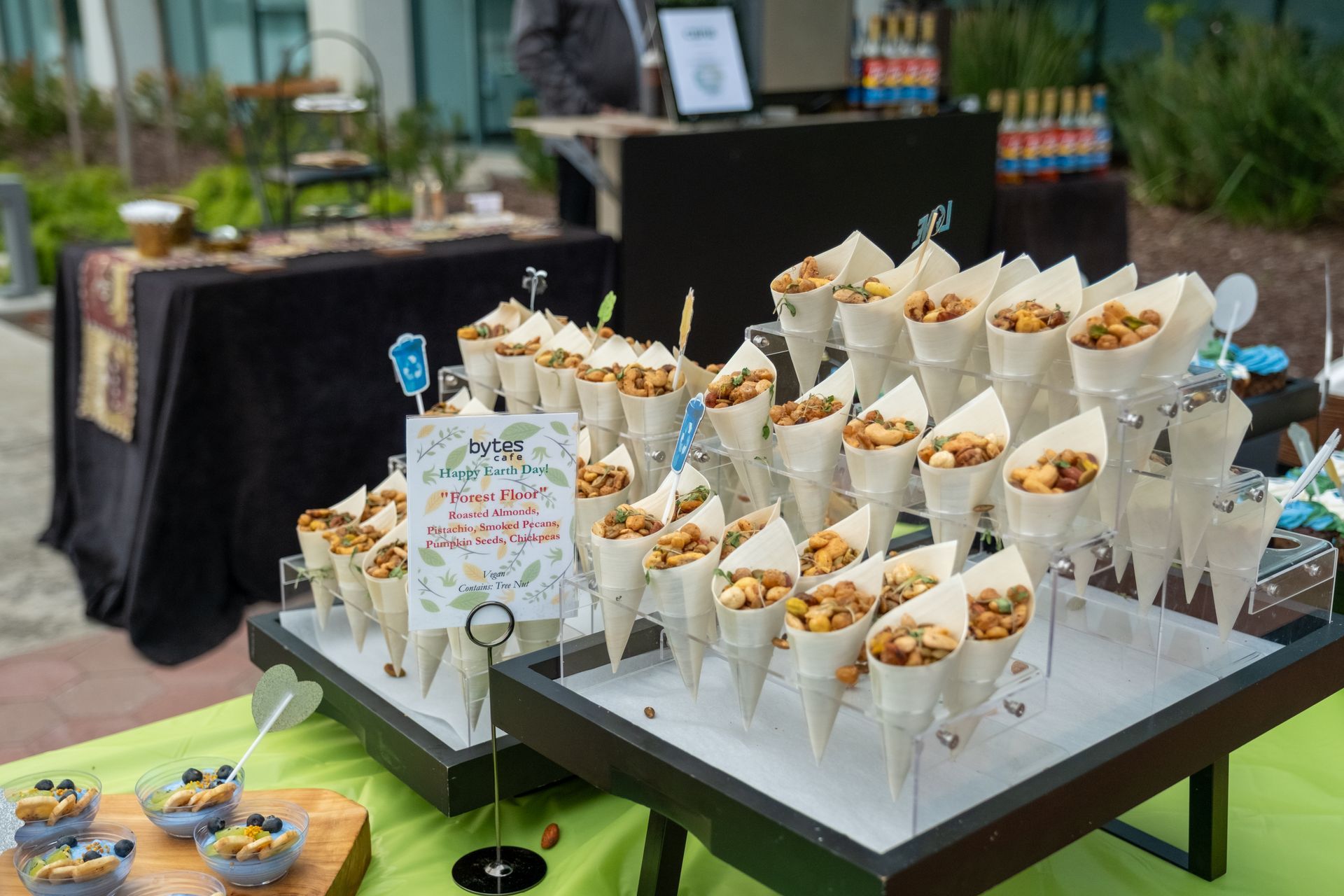Cones of snacks arranged on a table at an outdoor event, with beverages and other food items visible.
