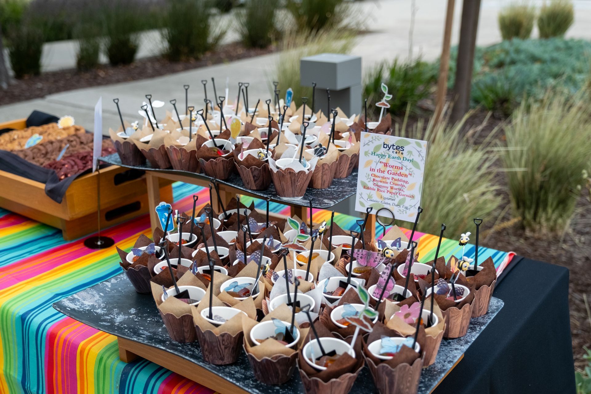 Dessert table with ice cream cups topped with decorations; a colorful cloth covers the table.