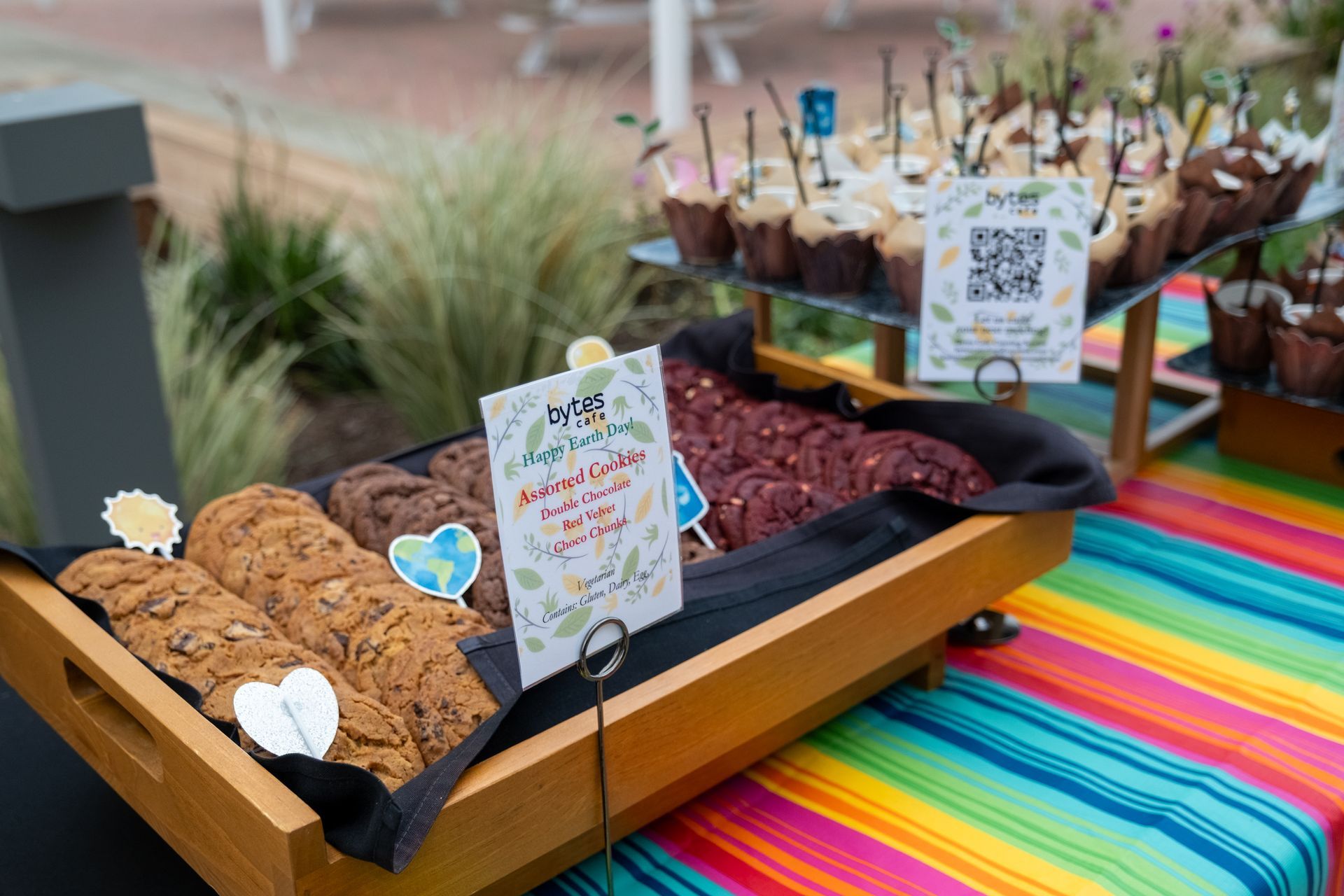 Dessert table with cookies and muffins; colorful striped tablecloth.