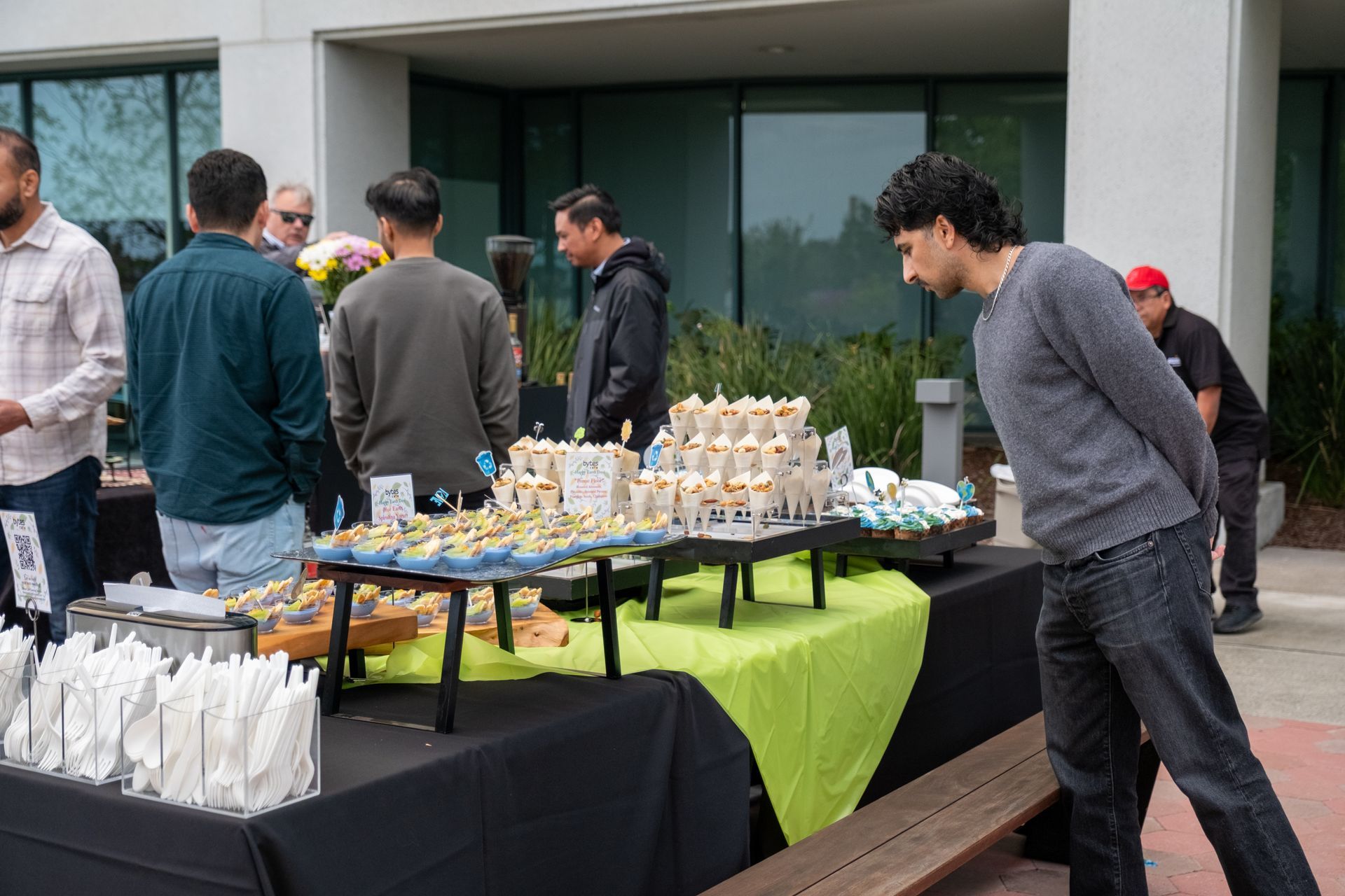 Outdoor event with food spread on tables; people browse the selection.