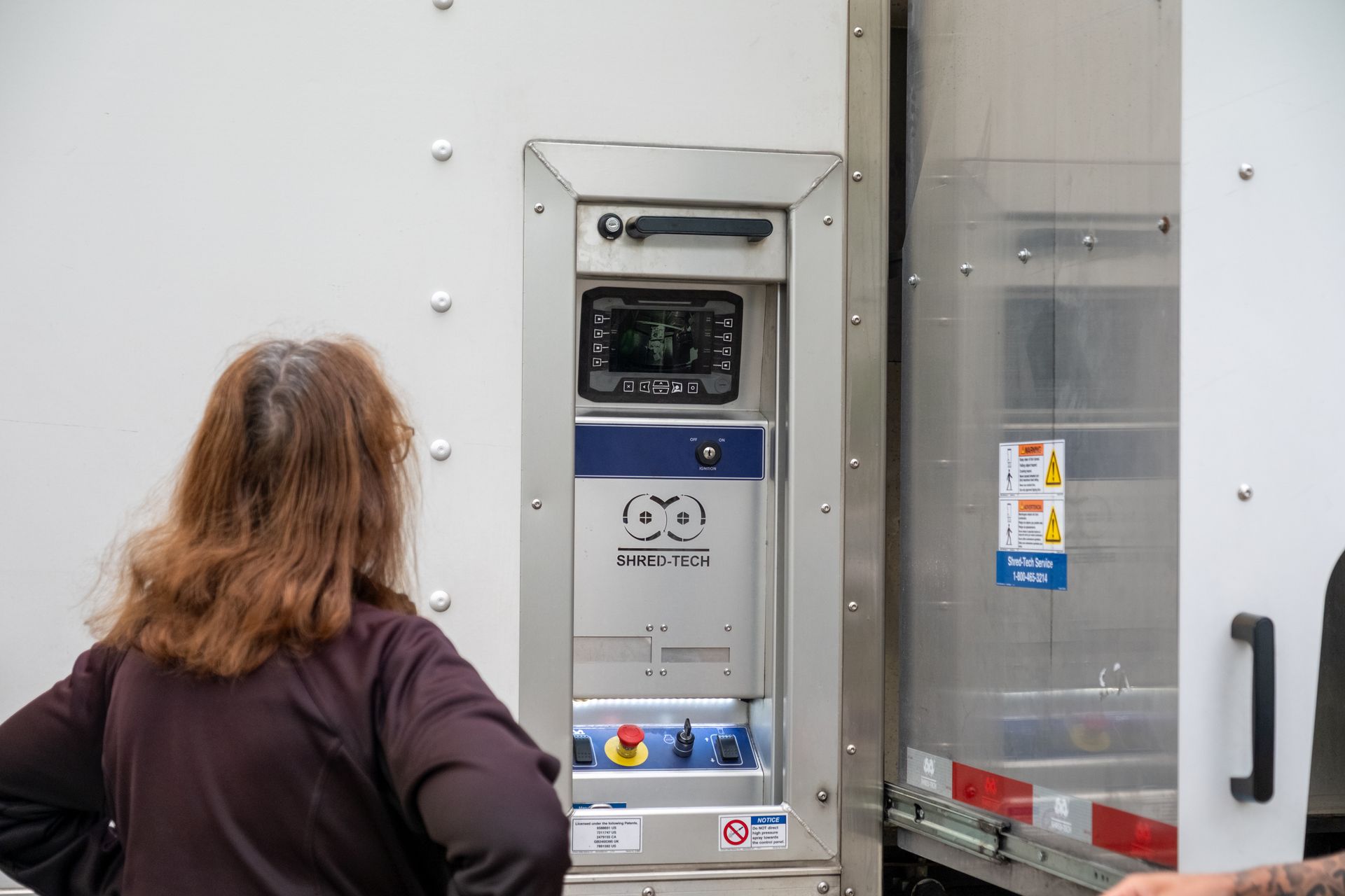 Woman looks at a control panel built into the side of a white truck. Panel has a screen and buttons.