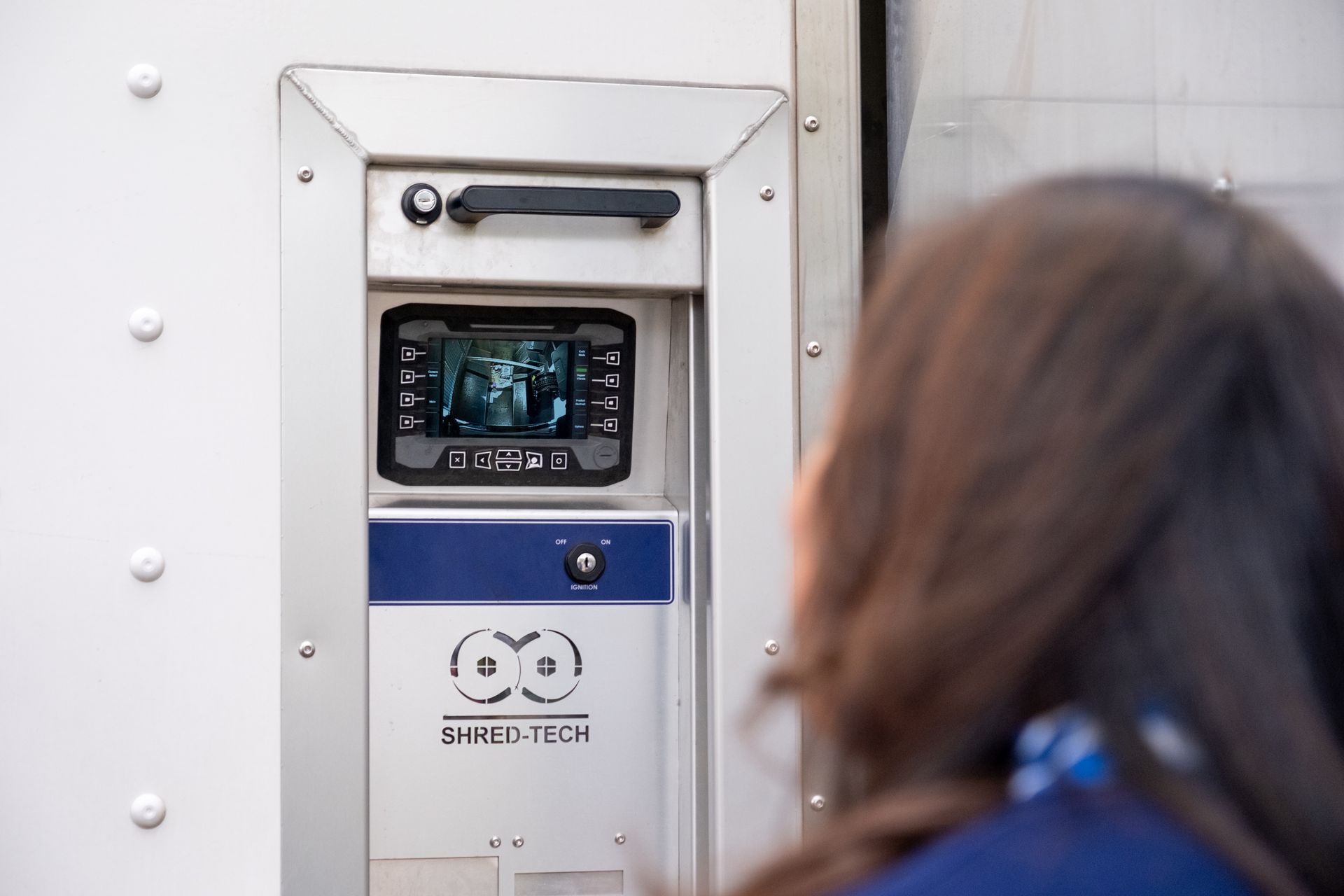 Woman looking at a screen built into a metal panel. The screen shows an image; on the panel are a handle and logo.
