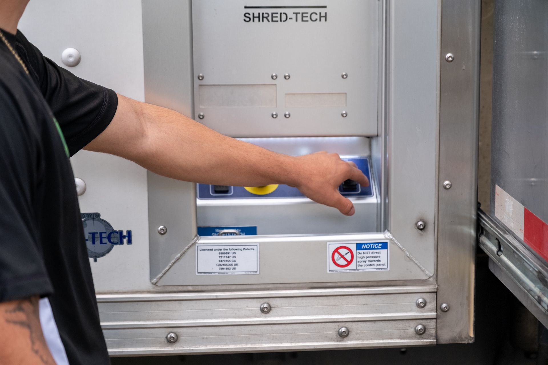 Person presses a blue button on a Shred-Tech machine, mounted on a truck.