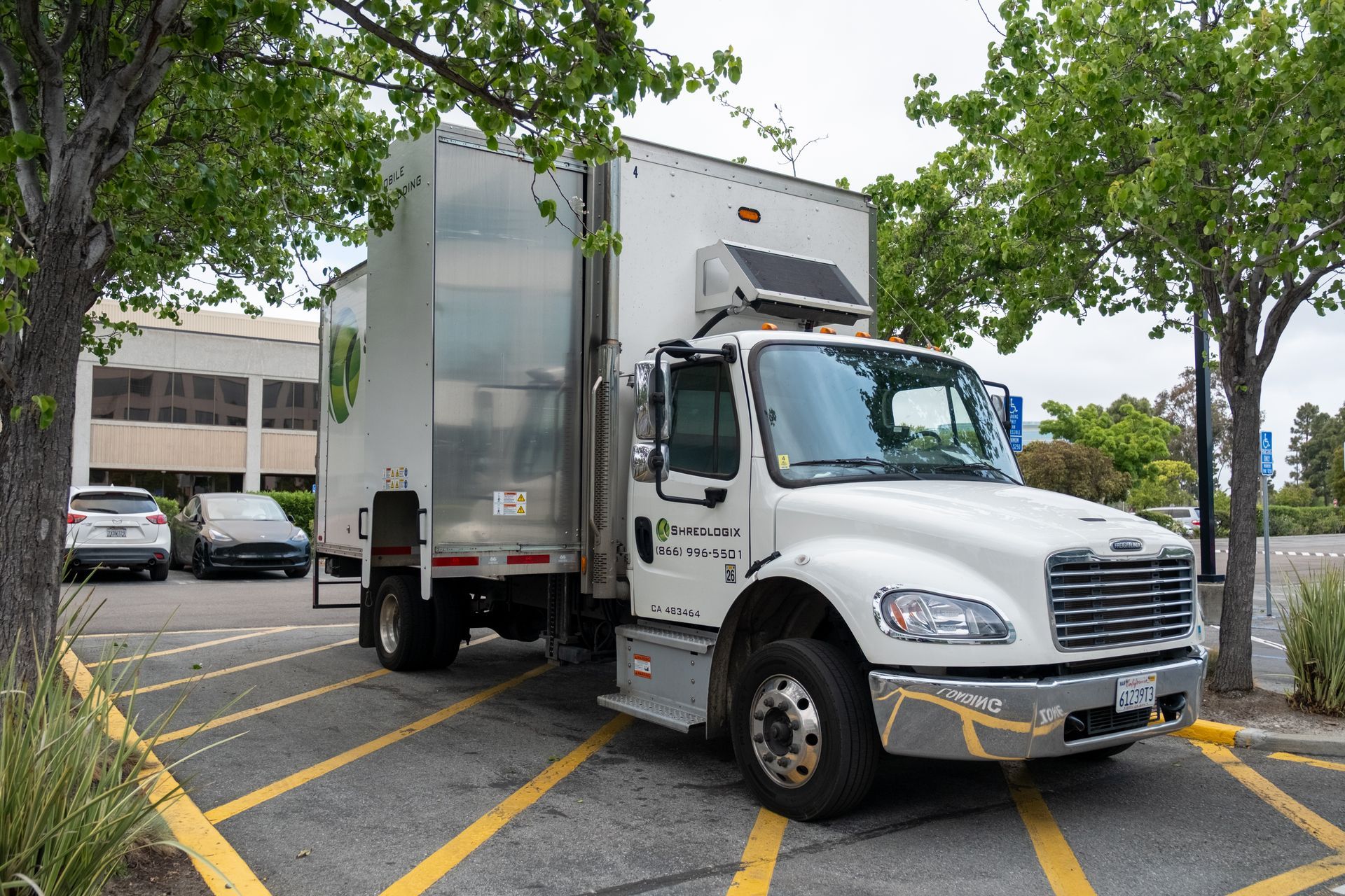 White refrigerated truck parked in a lot next to a building and trees.