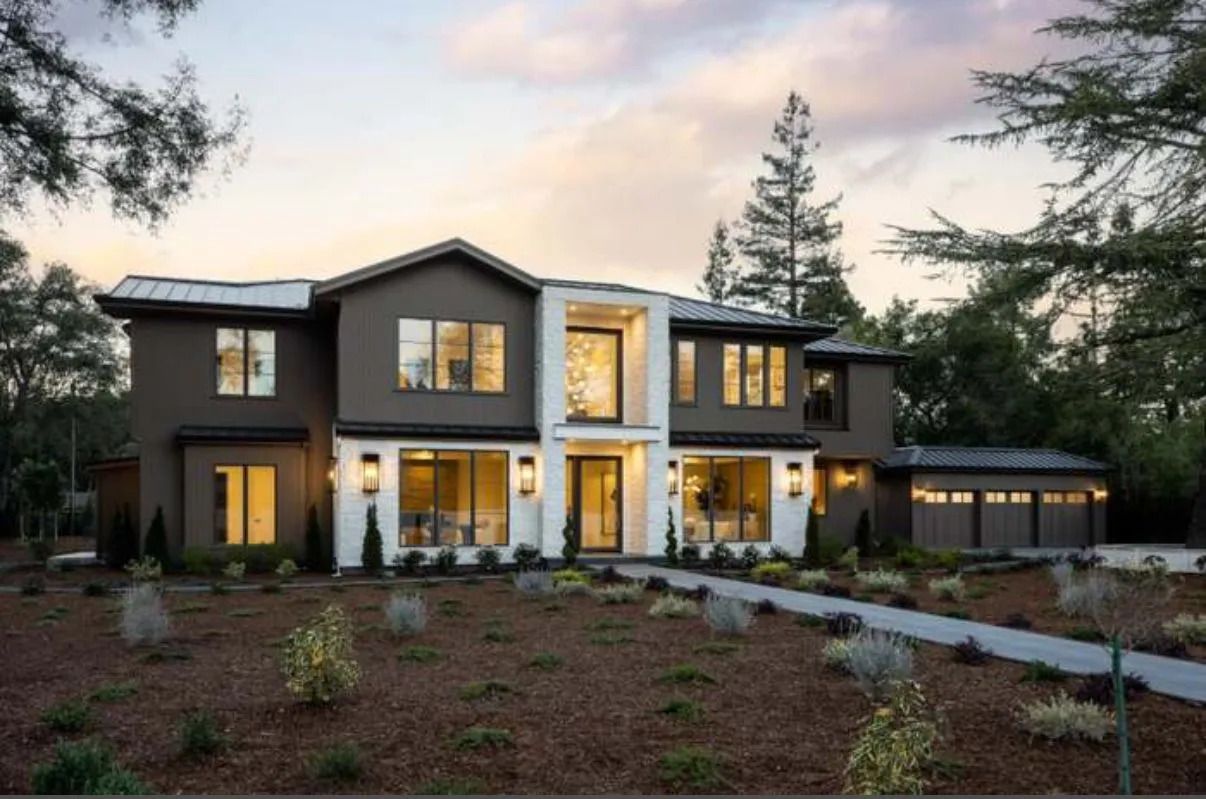 Modern two-story house with brown exterior, white trim, and a three-car garage. Surrounded by trees and brown landscaping.